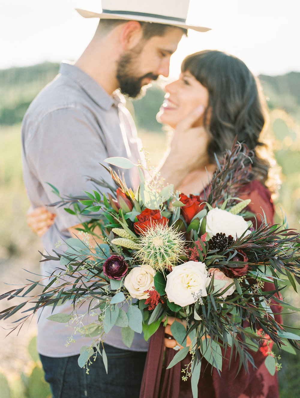  Couple smiling at each other with gorgeous desert backlighting on film and bridal bouquet in the foreground&nbsp; 