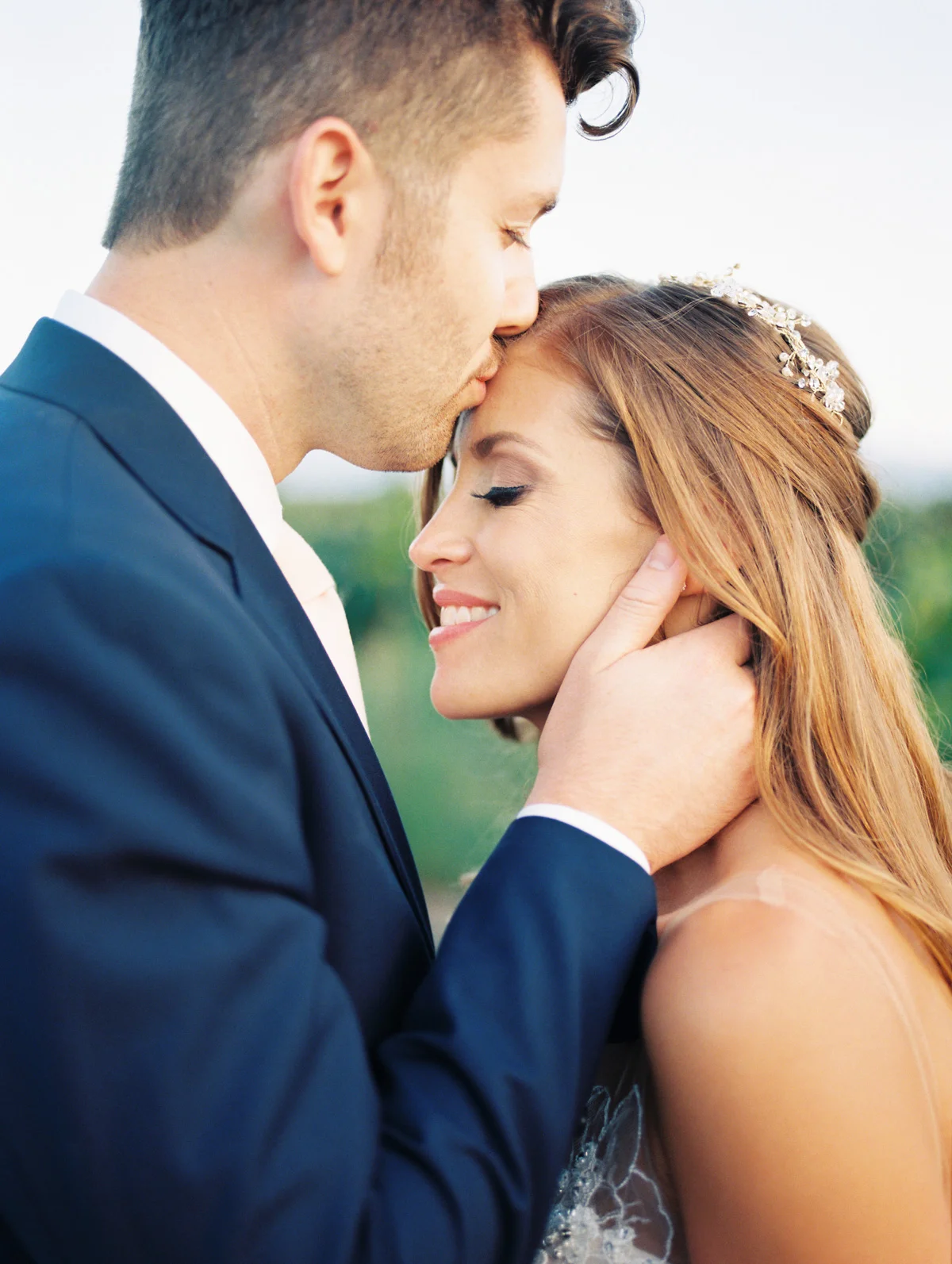 Groom kissing bride's head, bride smiling | Harrison & Jocelyne's gorgeous Temecula wedding day at Wiens Family Cellars captured by Temecula wedding photographers Betsy & John