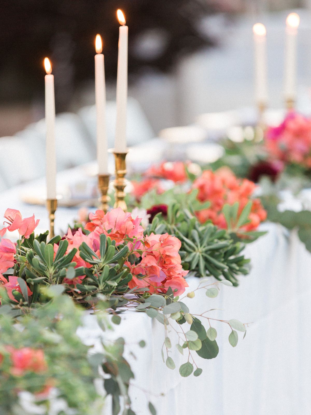 Beautiful head table settings with greenery, bougainvillea and brass candlestick holders 