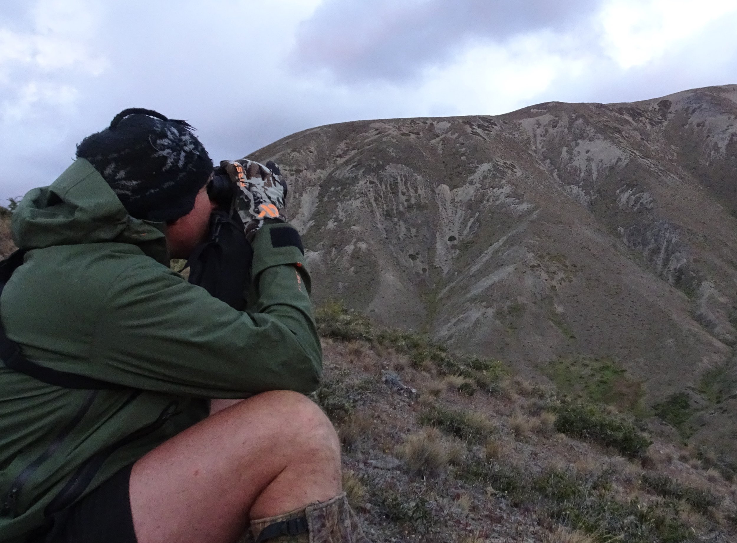  Shaun Monk sitting in the strong wind to spot into the sheltered gully heads, the First Lite merino gloves and the plain green  Seak Stormtight  packable jacket kept the showers and wind at bay. The jackets big under arm vents were great to zip open when climbing hard in the heat. 