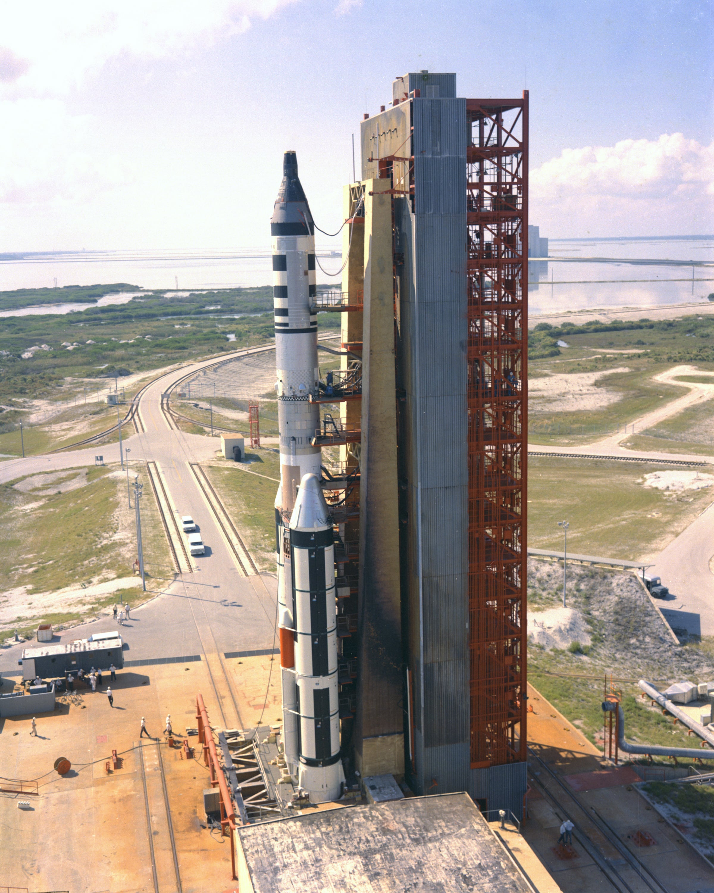 Titan IIIC number 9 is shown at Space Launch Complex 40 at Cape Canaveral Air Force Station. It was launched on November 3, 1966, as a test of the rocket. It also carried the Gemini 2 spacecraft, on its second suborbital flight to evaluate its heat shield as modified for MOL, and a simulated MOL canister carrying Air Force experiments. Note the similarity of the its umbilical tower to that in Painting #7. (Photo PL66C-76206, USAF)
