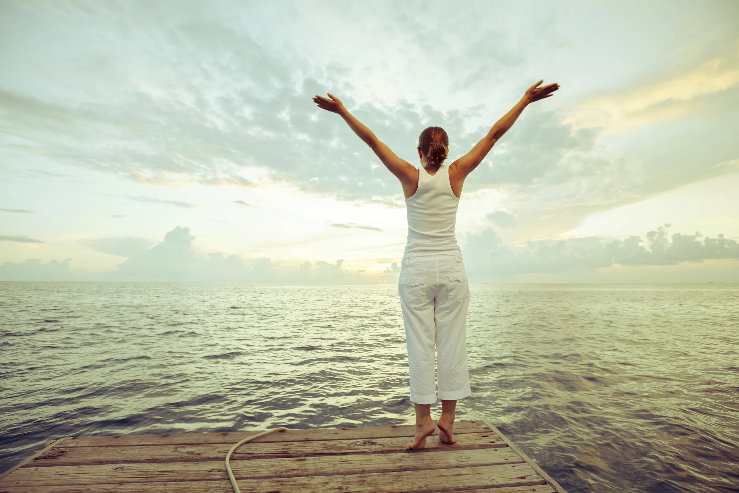Woman with arms stretching up, looking toward ocean.
