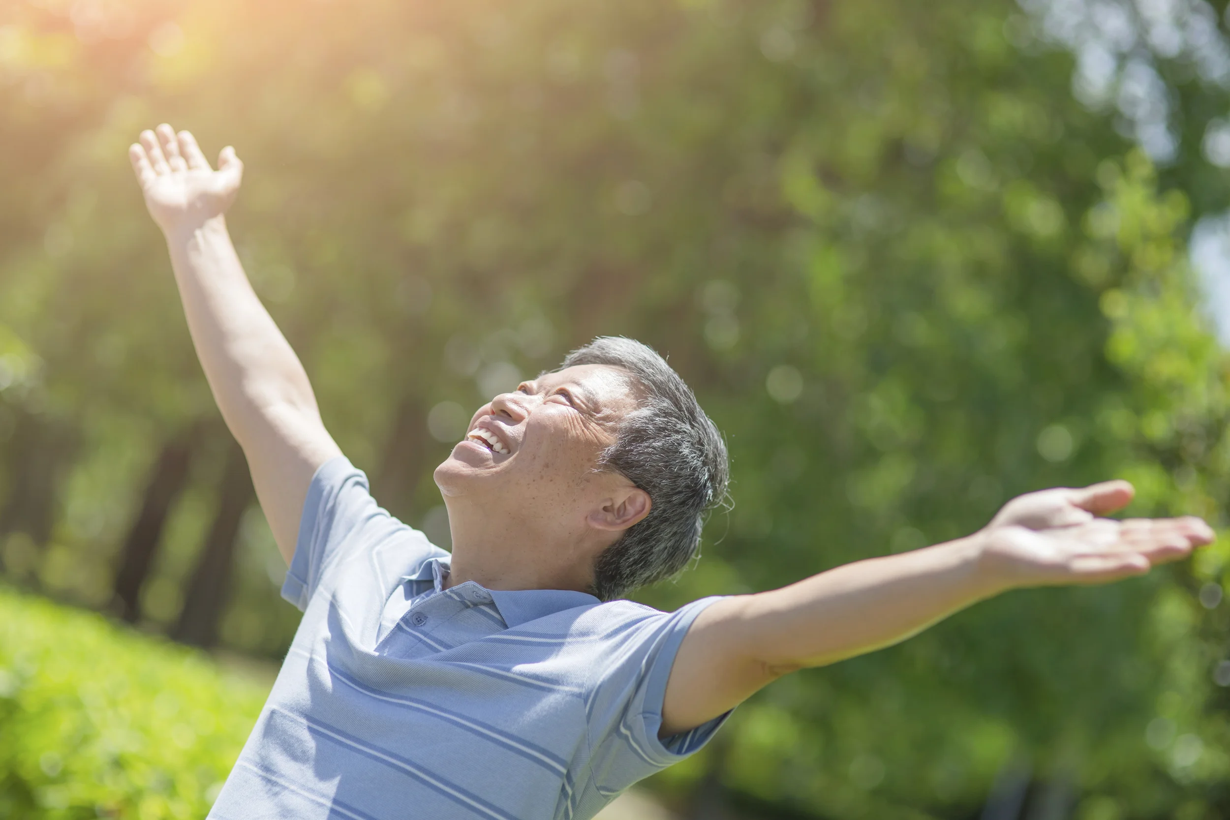 Man with raised arms, smiling, looking up at sky.