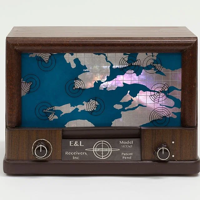 Radioscope (Instrument #4): Found radio box, plexiglass, paint, lexan, polyester, silver tape, projected video. 9"w x 13"h x 9"d From Global Institute of Ambiguous Instruments database: Radioscope Function: Prior to the 1964 discovery of cosmic microwave background radiation (CMB) by radio astronomers, Robert Wilson and Arno Penzias, other amateur radio astronomers were listening to and collecting information from faint radio signals coming from deep space. These astronomers were using earlier instruments, often handmade, like this Cosmic Radioscope. At that time, solid theory about CMB and its origins did not exist, leaving each amateur astronomer to speculate broadly about the origins of these signals. Because the signals seemed to originate from all directions in the cosmos, some believed the waves might relate to astrological theory. Others, more correctly as it turns out, speculated that the waves had something to do with the origins of the universe itself. This early Radioscope, has both a rear and front display screen. The rear screen is a projection of the current cosmic weather. The front screen consists of a cosmic map for a small sector of the Milky Way galaxy. A series of dials represent yet smaller sectors. Because these microwave signals are both weak and sporadic, each dial moves almost invisibly upward or downward as detection occurs. It is theorized that this instrument was built by an amateur radio astronomer, perhaps as a prototype for commercial market. No patent application has yet been founddespite the claim on its label that a patent is pending. Inventory # 49-19CRS