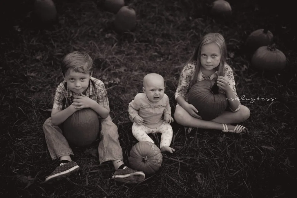 three kids sitting with pumpkins