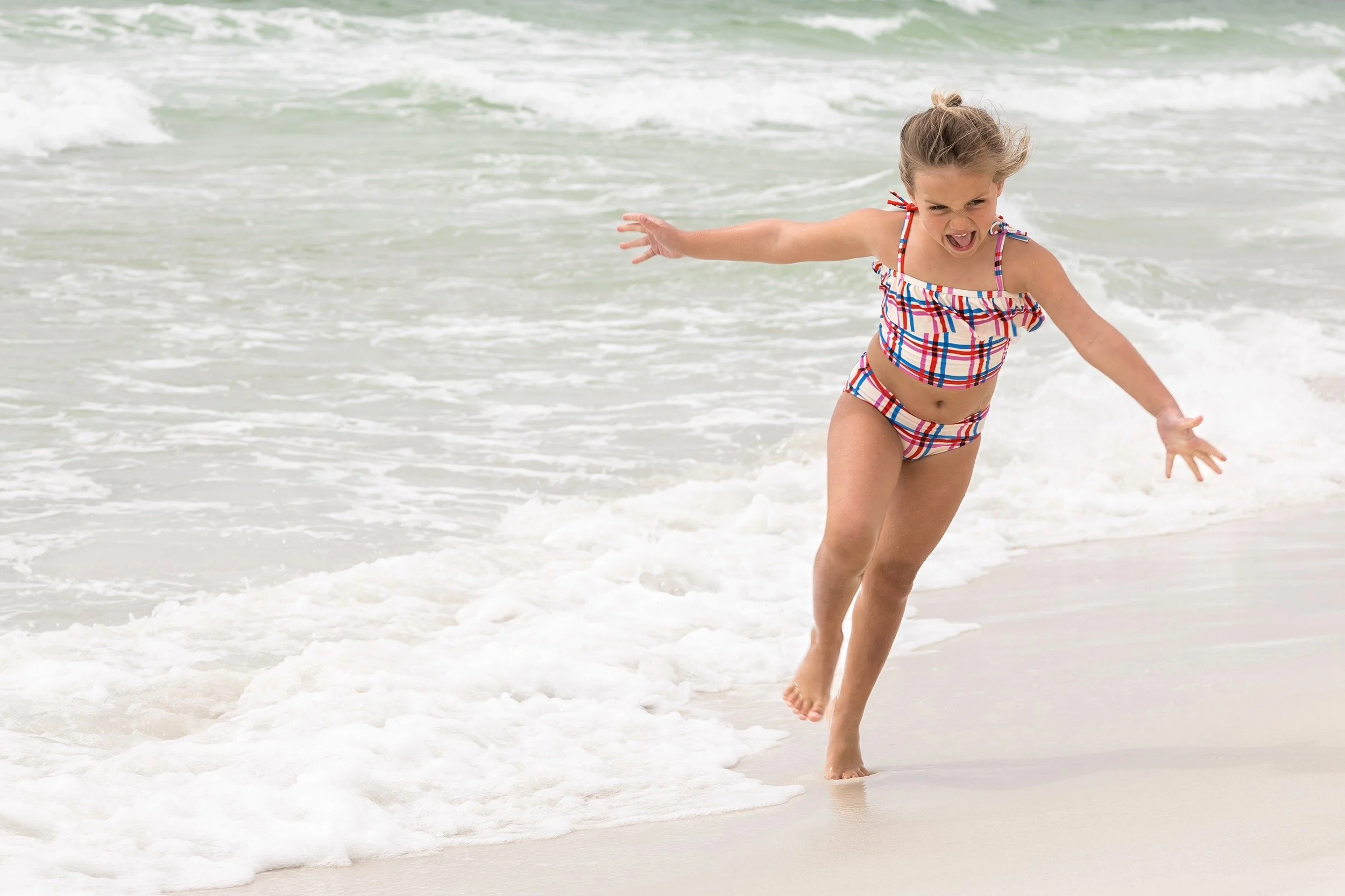 Candid family photography at WaterSound Beach Florida showing a young girl running along the shoreline.