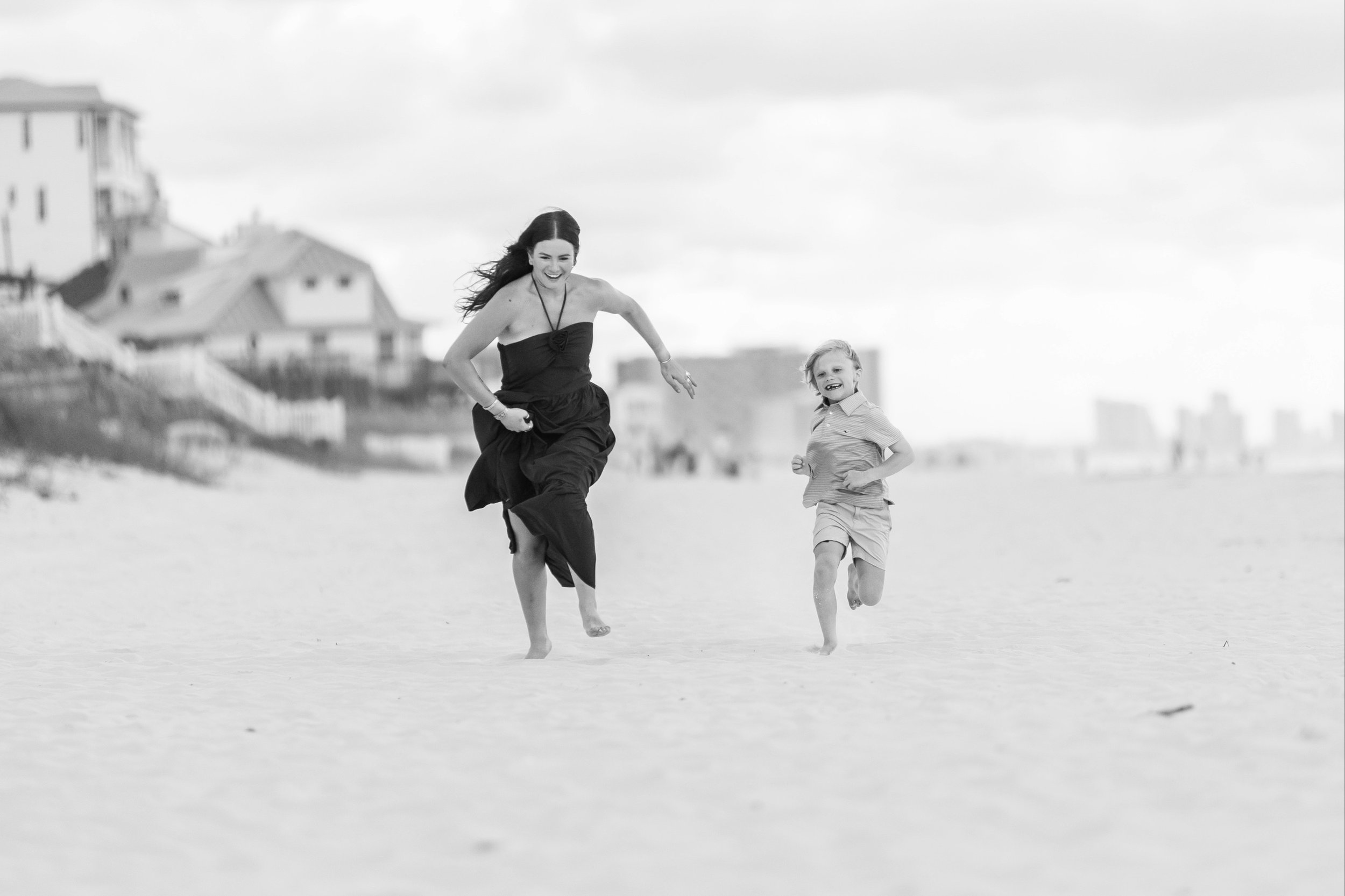Black and white documentary photography of a sister and brother running on the sand during a Rosemary Beach family photo session.