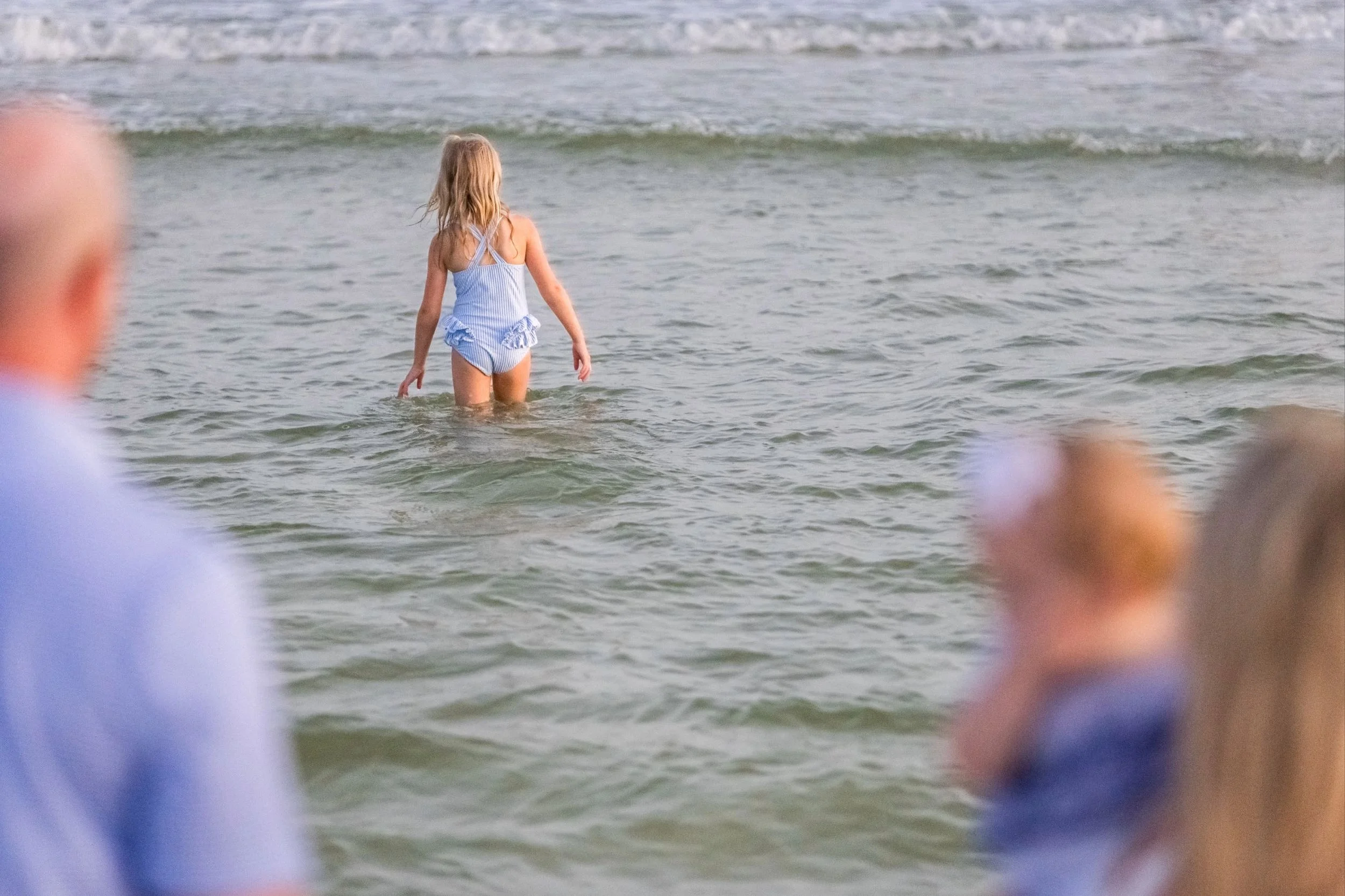 Family at the beach for photography session watching little girl playing in the water.