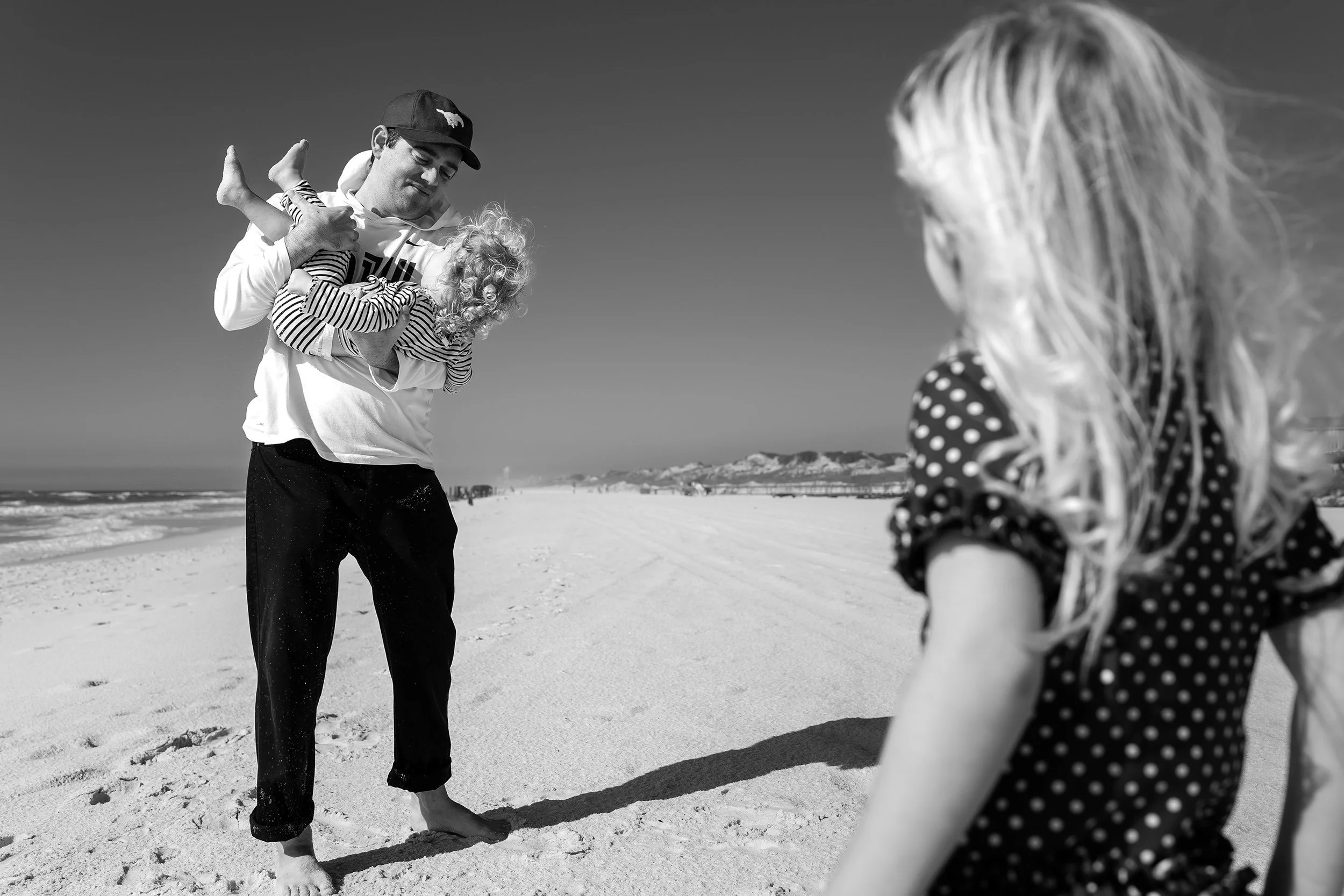 Unposed family photography session on 30a of a dad holding a toddler with the sister watching.