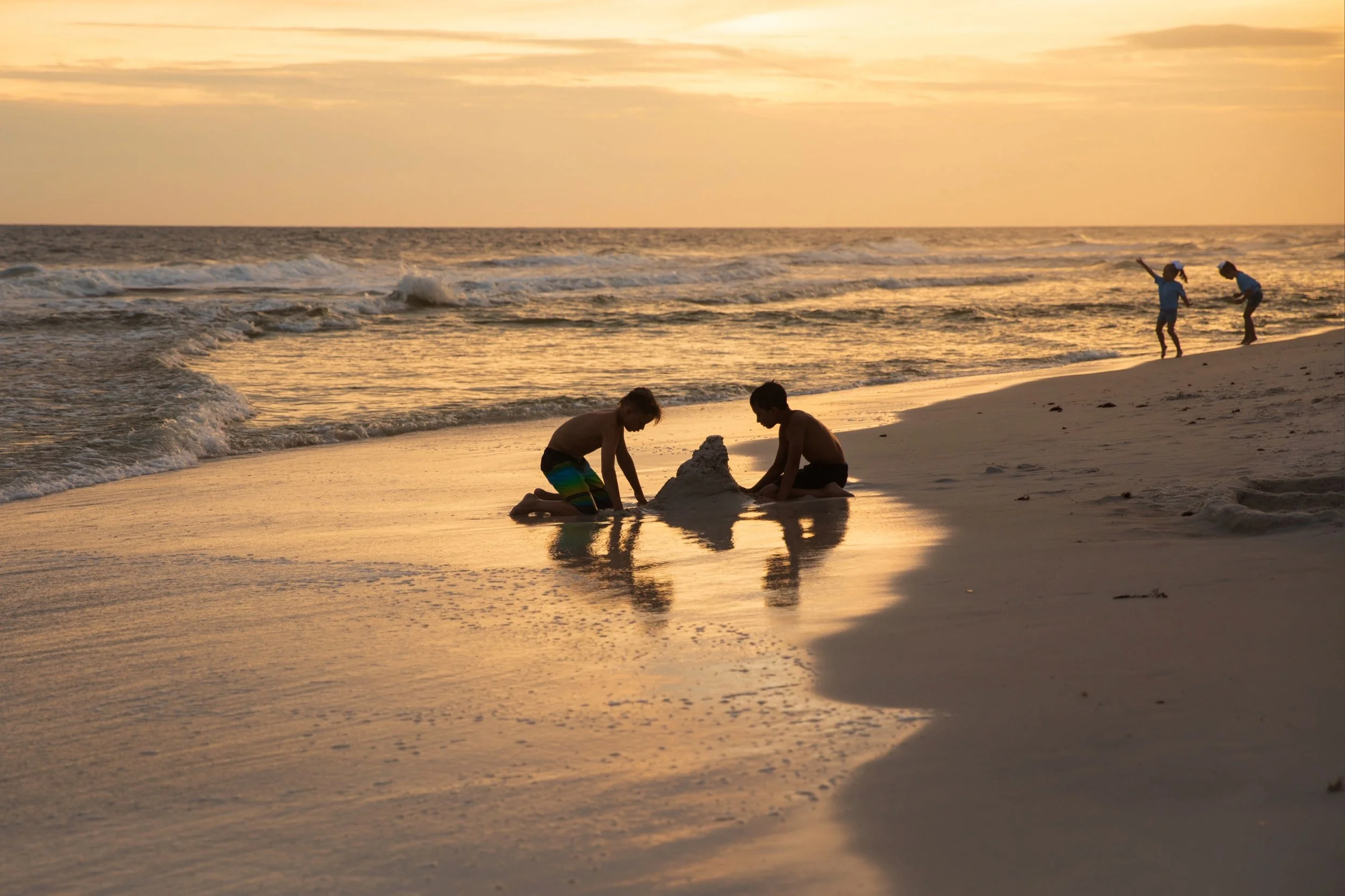 Children building a sandcastle on a 30A beach at sunset