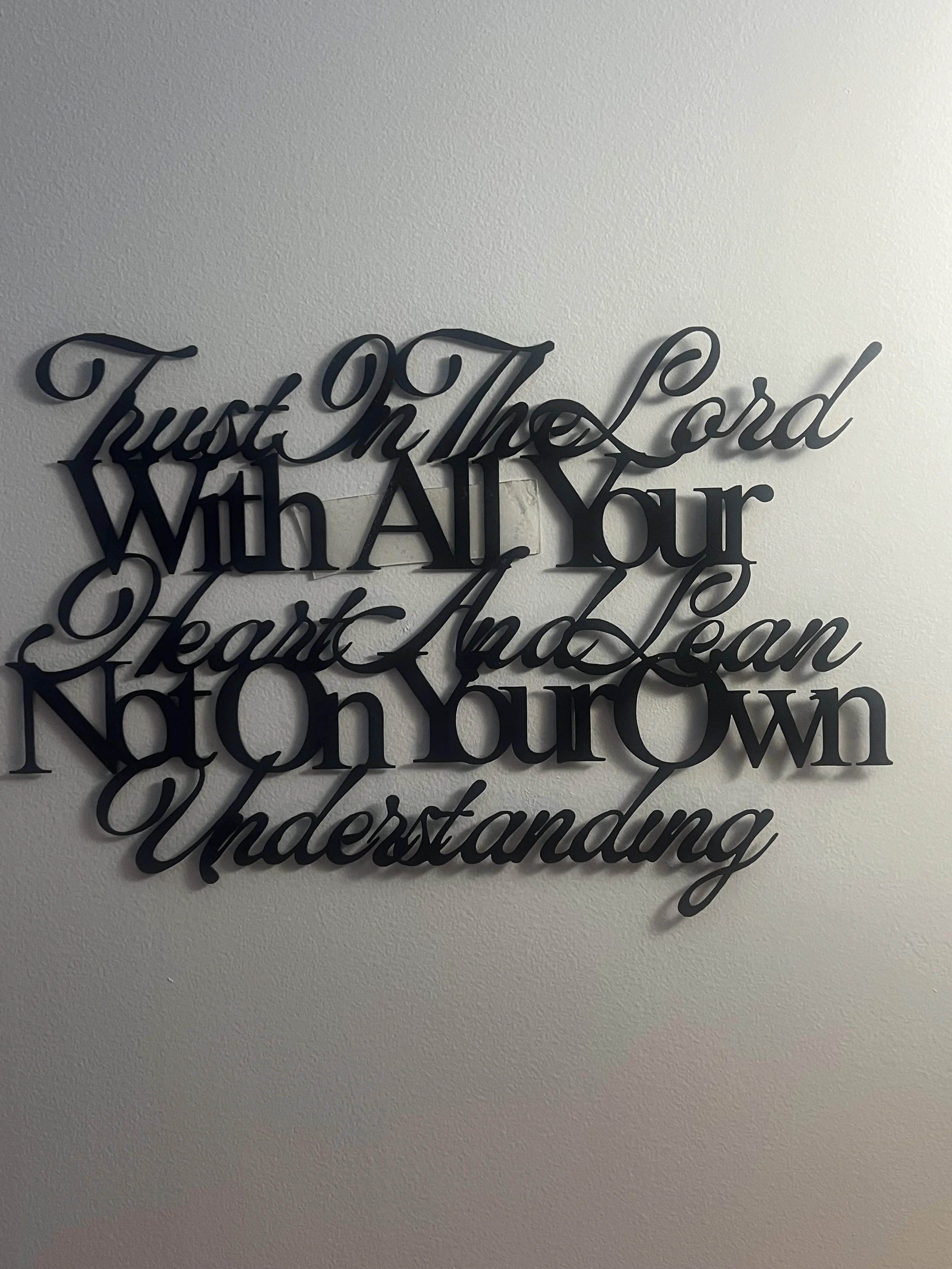 Decorative wall sign with the quote 'Trust in the Lord with all your heart and lean not on your own understanding' on a plain white wall.