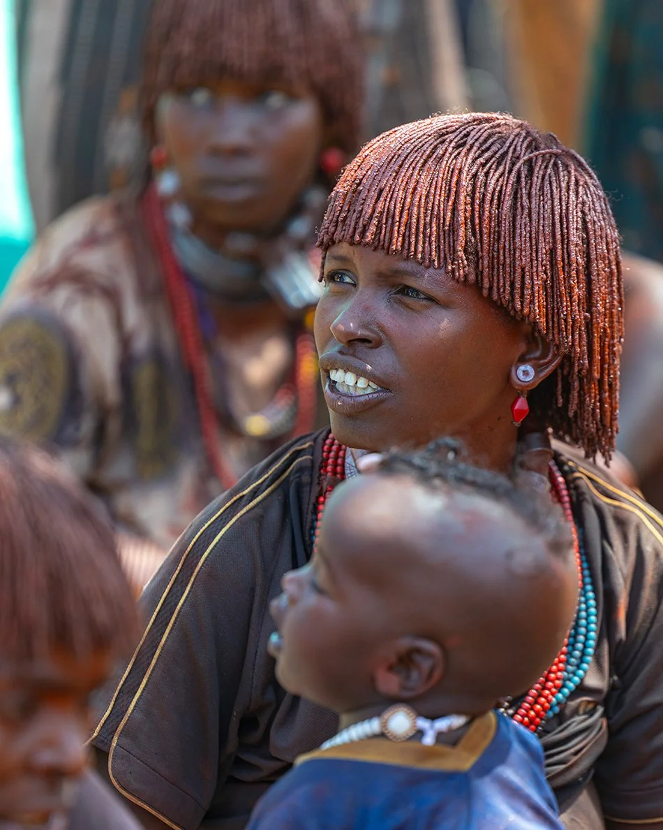 Die Hamer Frauen haben alle die gleiche Frisur. Sie gestalten das Haar und die Haut mit spezieller roter Lehmerde. Weiterhin tragen viele Narben auf der Haut. Die Erstfrau ist an einem besonderen Halsschmuck aus Leder zu erkennen. Dieser wird am Tag
