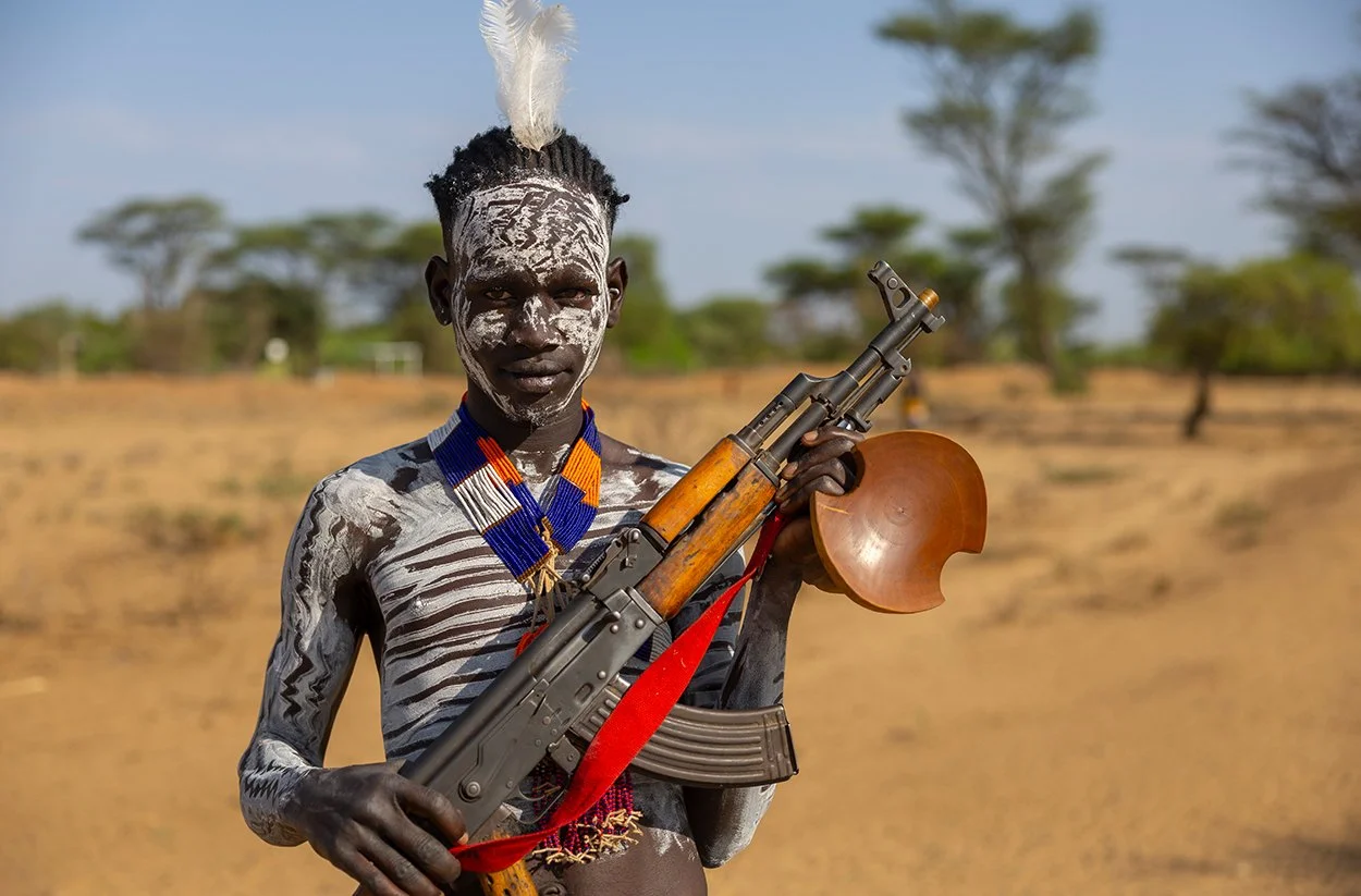  Kara Mann mit Sitzhocker und AK 47 