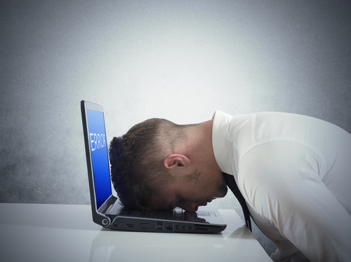 Photo of a man with his forehead planted onto an open laptop computer's keyboard