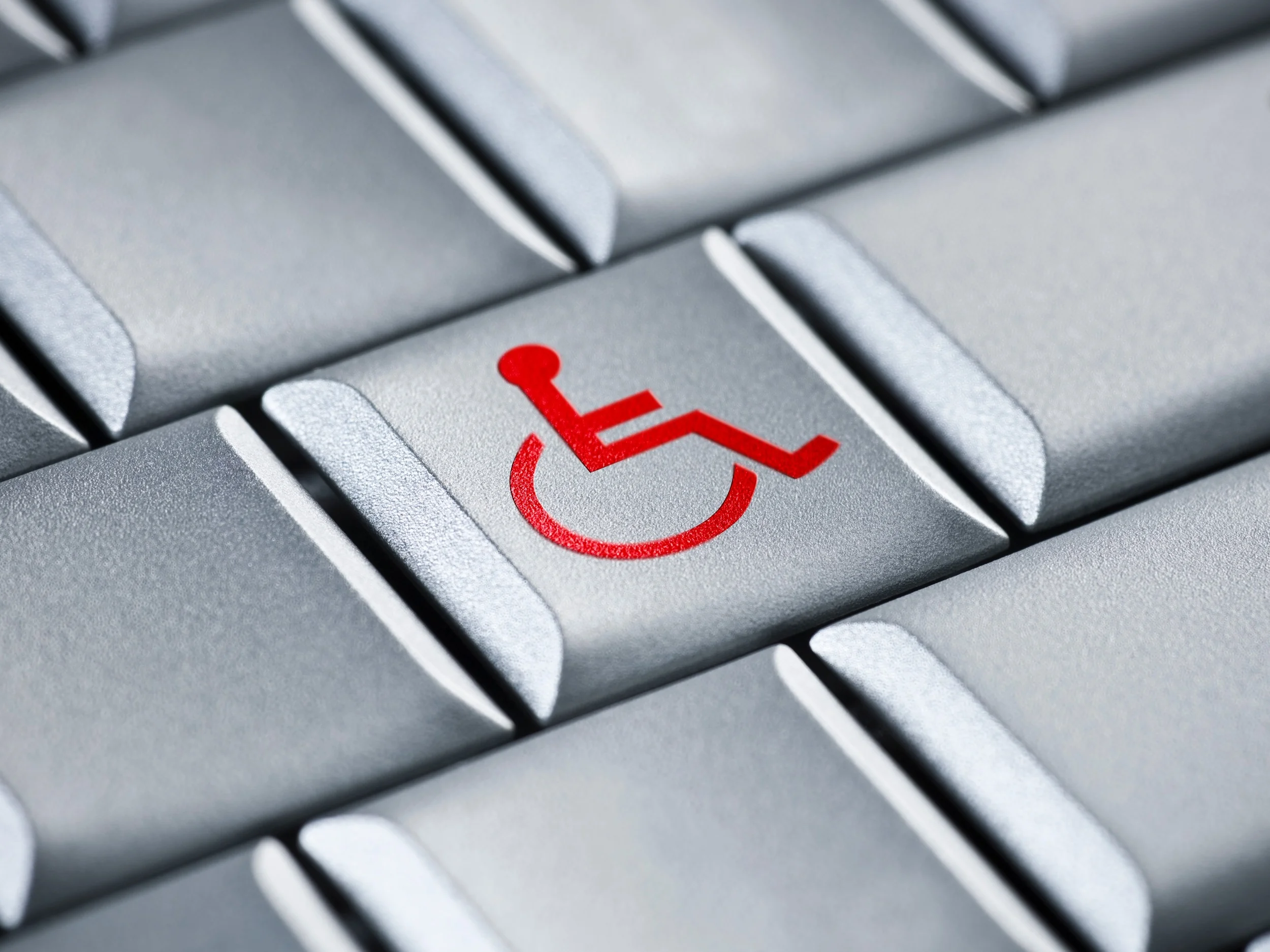 Closeup photo of a gray computer keyboard with a red wheelchair symbol on the middle key