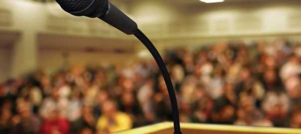 Photo of a crowded audience, viewed from behind a speaker's platform and microphone