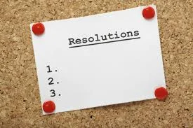 Cork bulletin board with a white rectangular piece of paper pinned to it, reading: Resolutions 1., 2., 3.