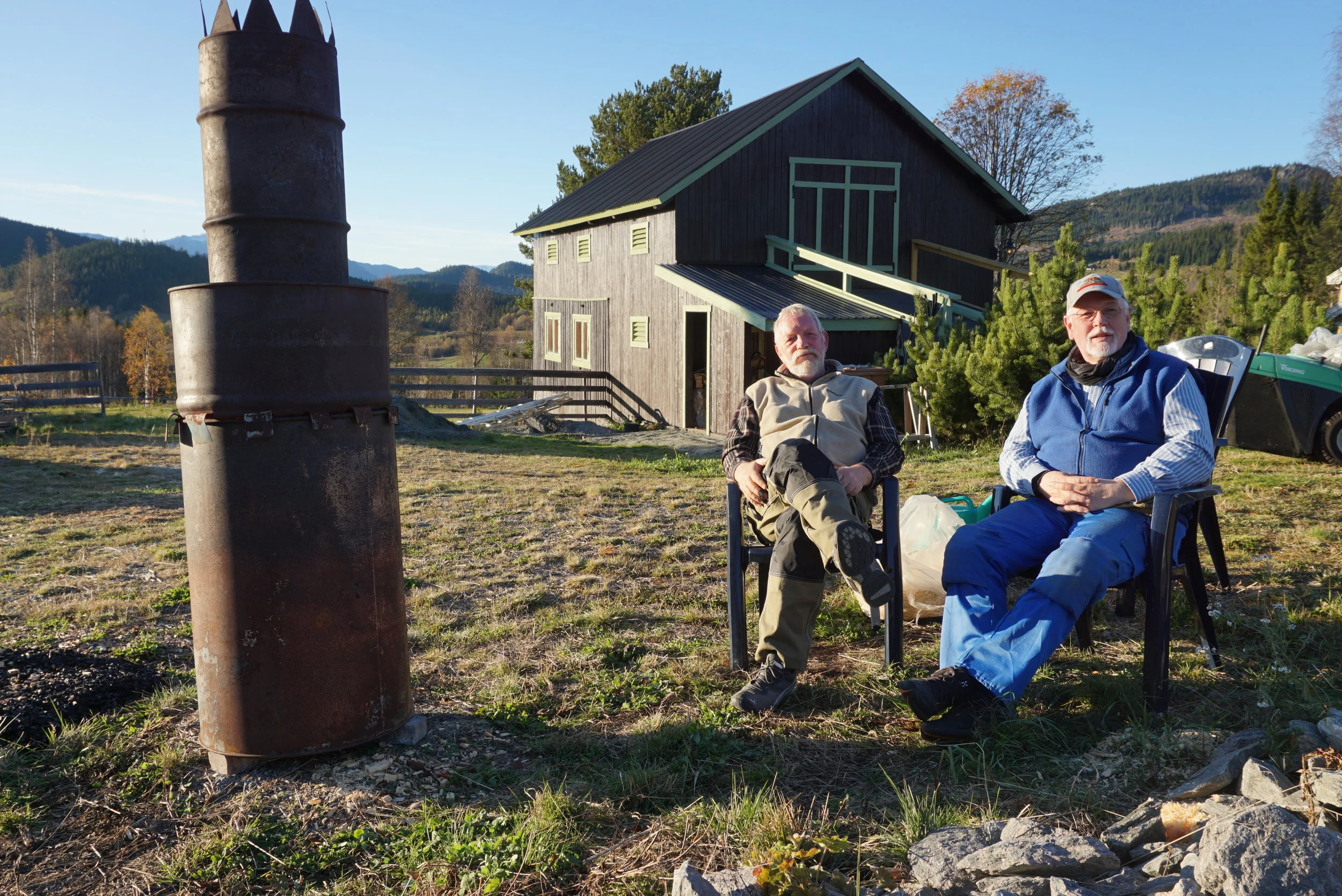 Kullbrenning i kveldssola på Karskogen. Olav th. og Knut Arne tv. har gjennom et langt liv sammen, bygd opp småbruket Karskogen til å bli et sted for utvikling av god jord. Med fokus på kompostering, biokull og livet i jorda ser de resultater de tro…