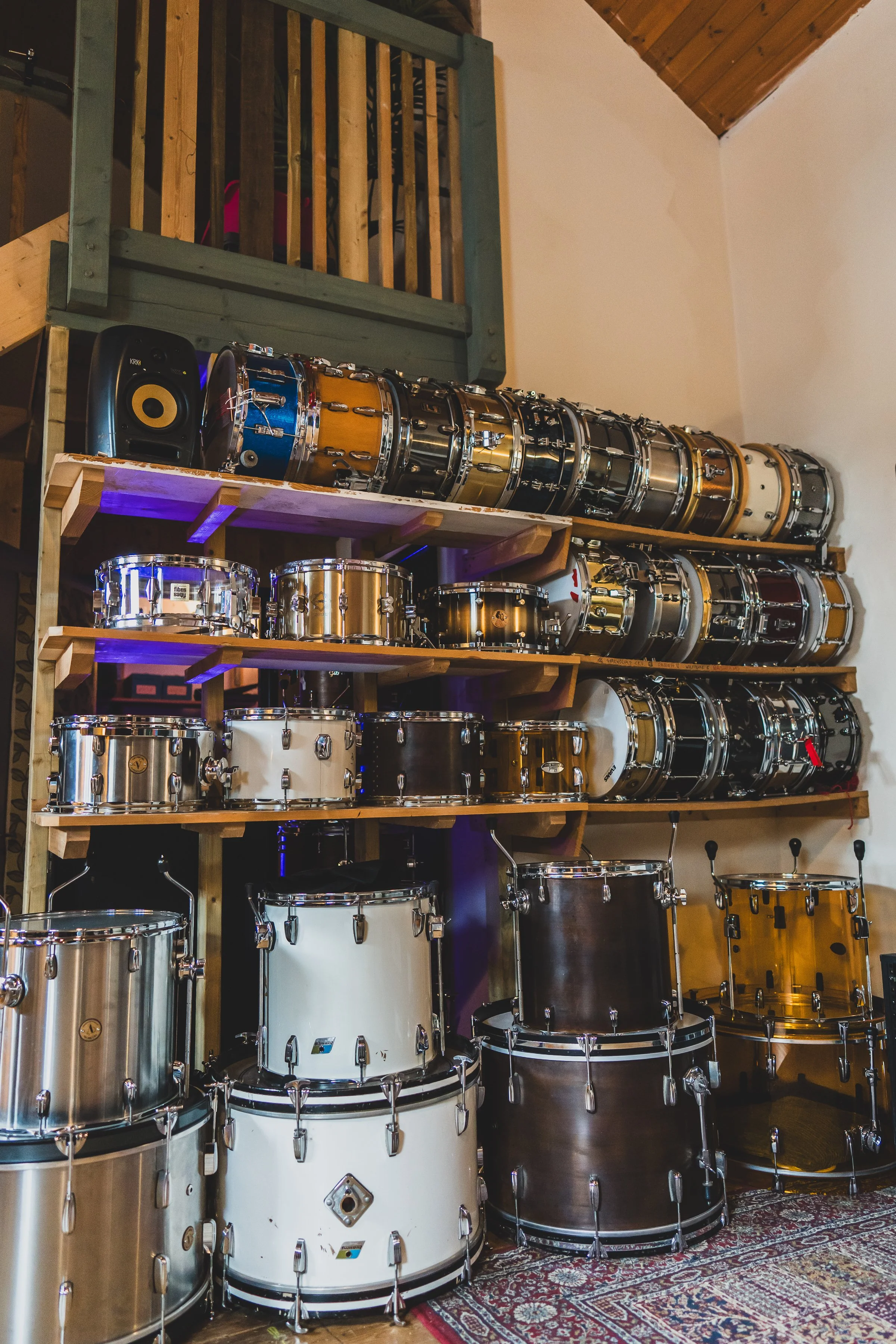 Collection of various drums stacked on wooden shelves in a music room.