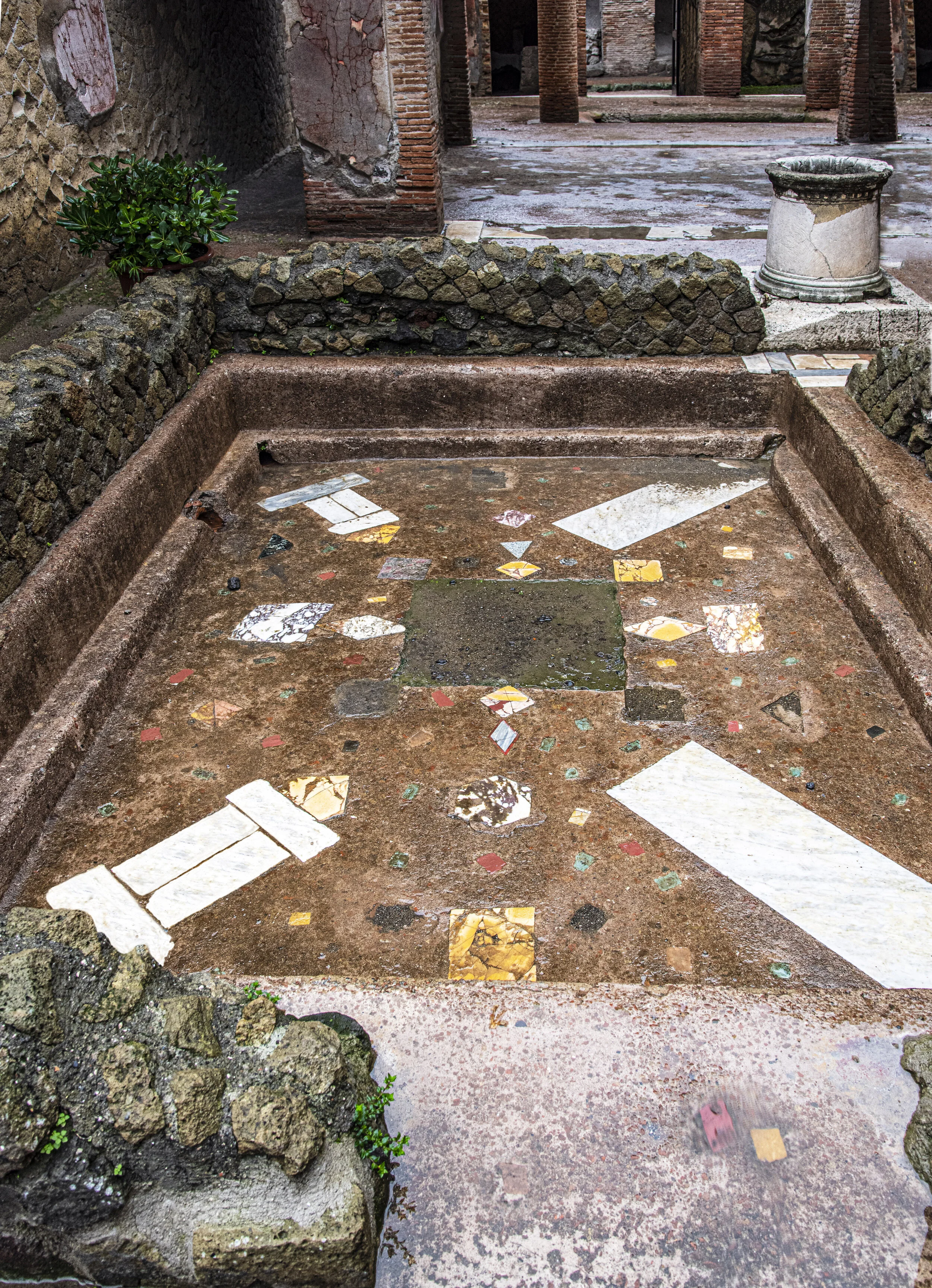 Casa dei due Atri second atrium features this cocciopesto pool decorated with strips of polychrome marble set around a central slot that once housed a fountain statue. On the edge is a marble puteal