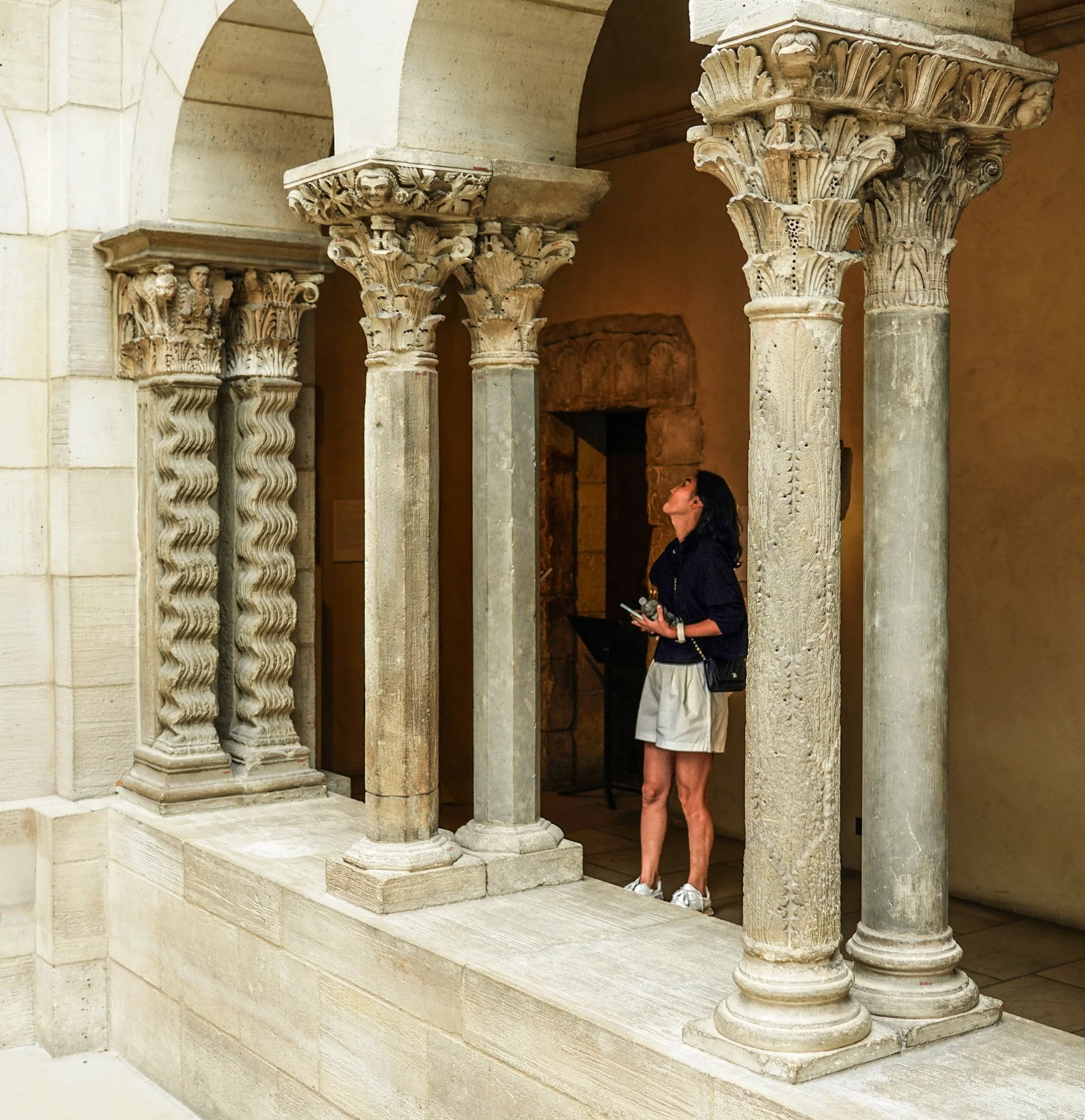Courtyard East arcade: masklike head in delicate naturalistic grapevine on the abacus block, middle column.