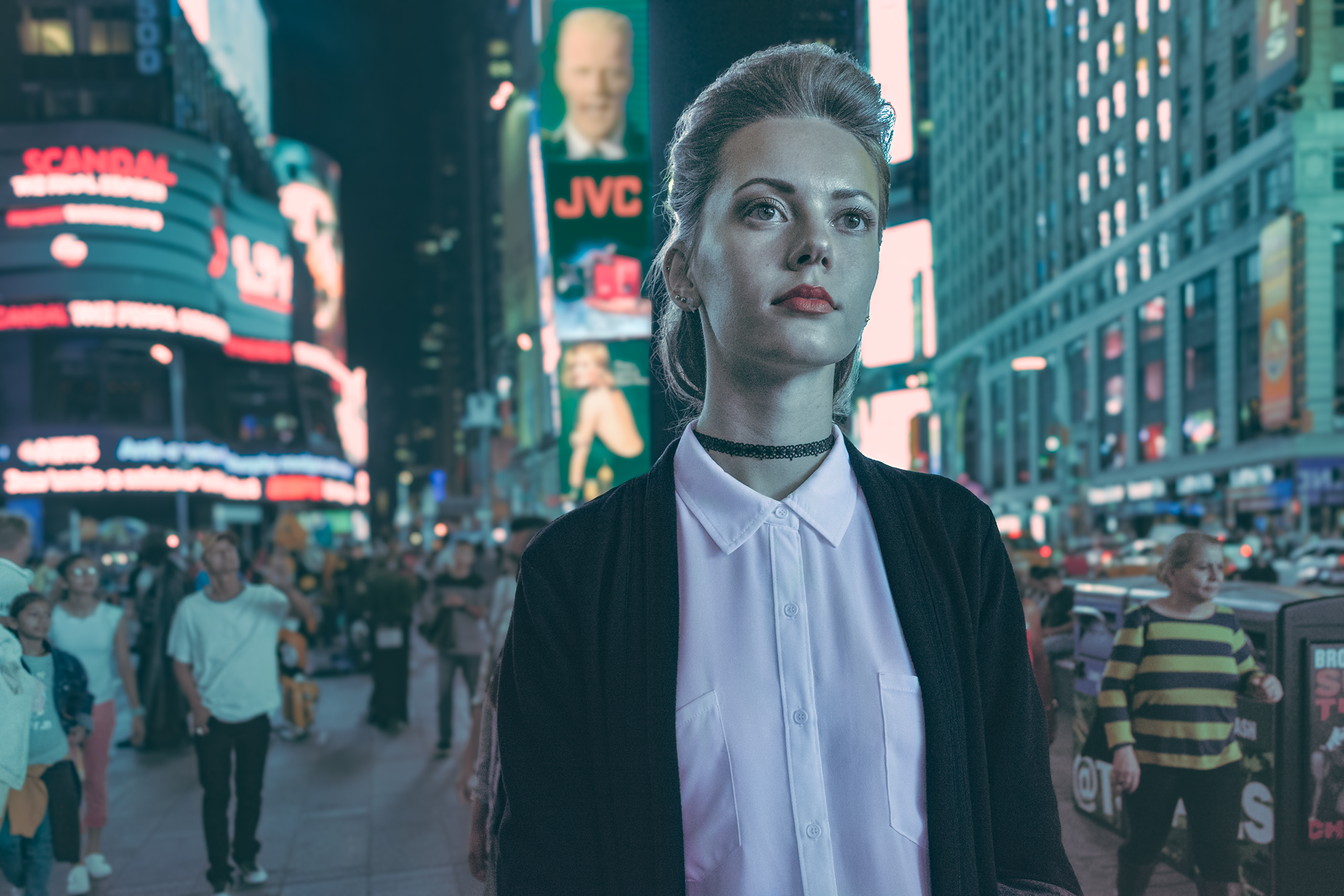A woman with blonde hair in a ponytail, wearing a white button-up shirt, black choker, and dark jacket, stands in Times Square at night with bright billboards and a crowd of people around her.