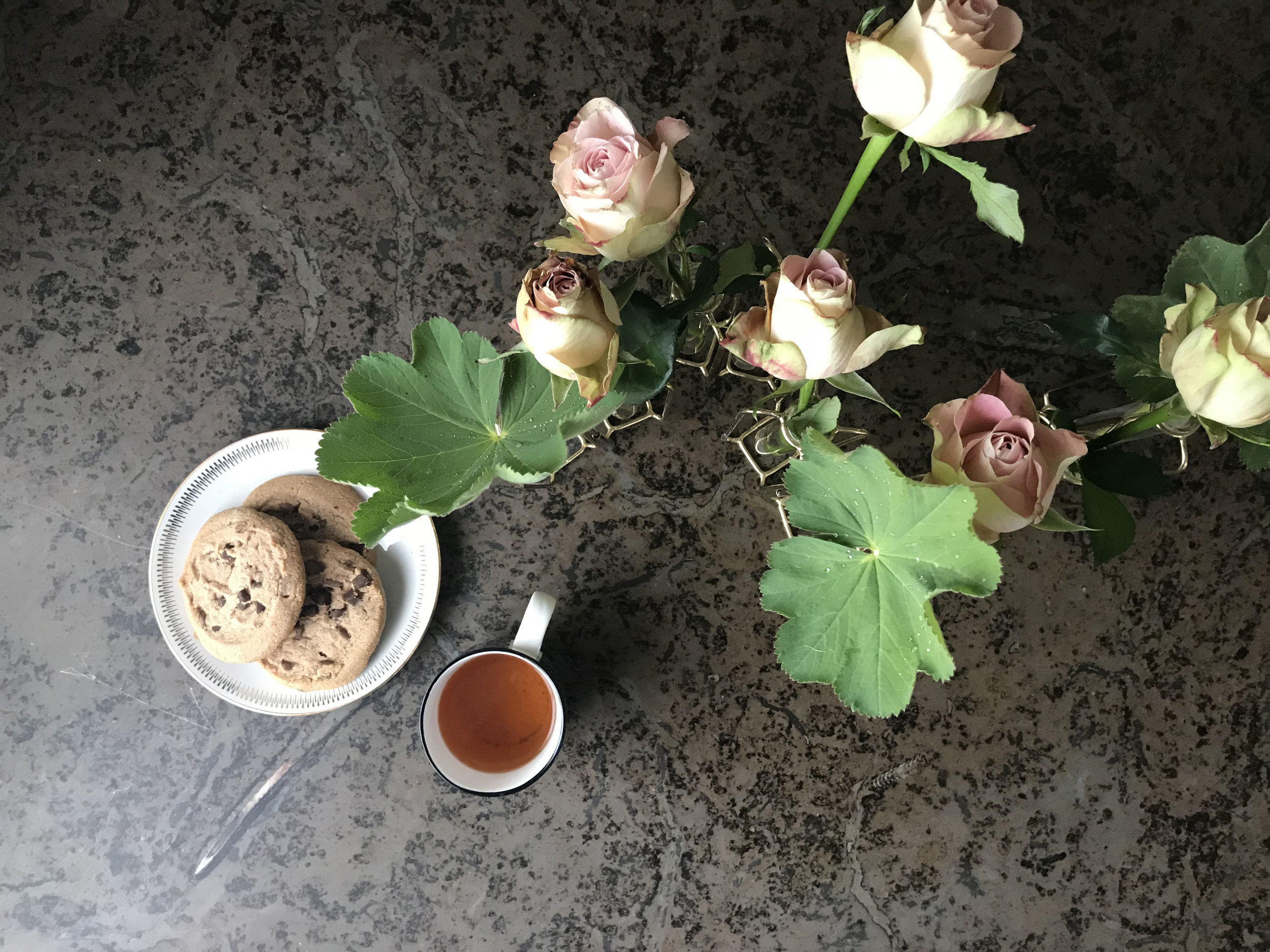 Blommor, kopp med te och fat med kakor på mörk stenskiva