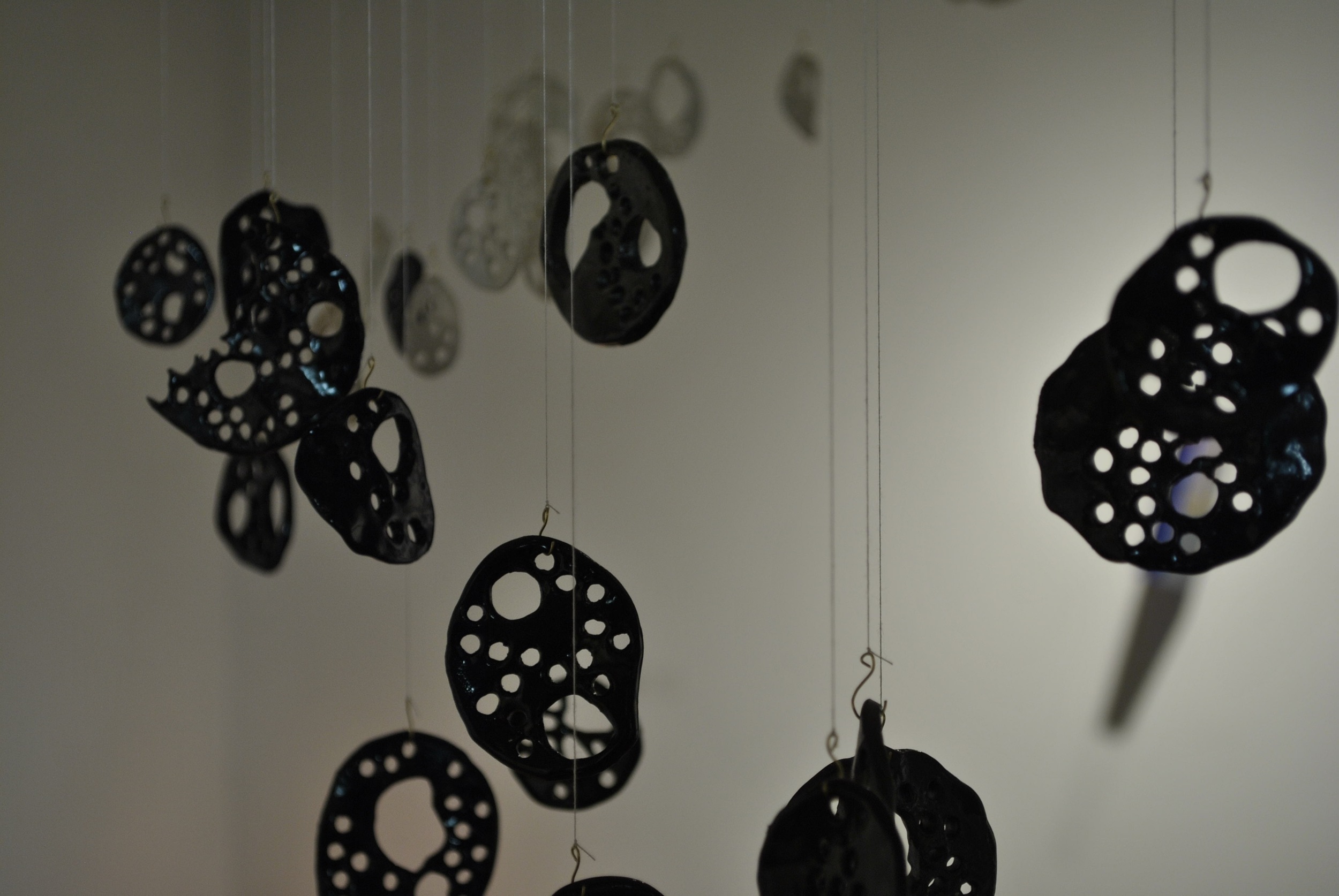Black ceramic circles with organic holes hanging from strings in Boston MA Shannon May Mackenzie photo