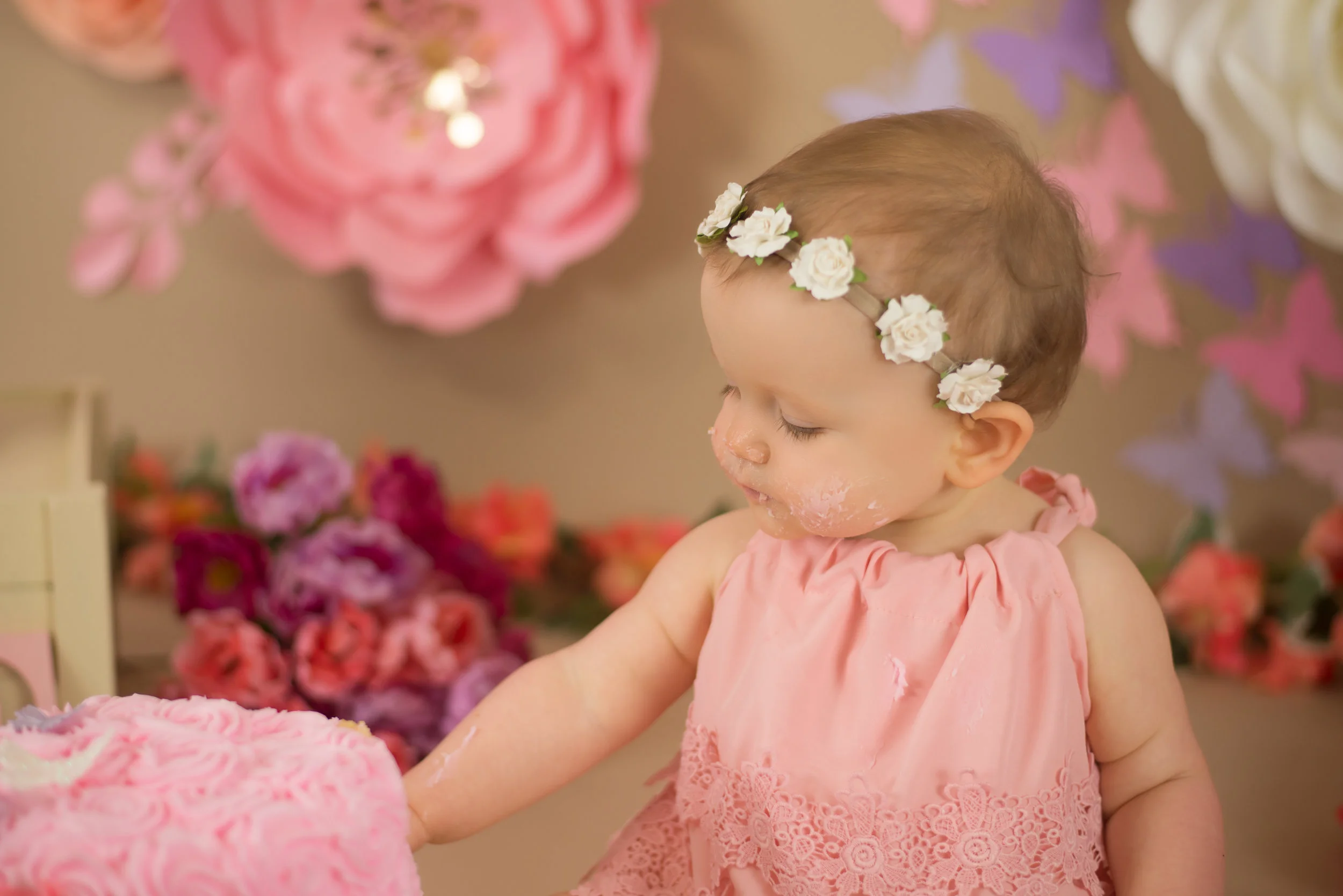 baby girl wearing pink eats cake surrounded by flowers during cake smash in Wilmington nc