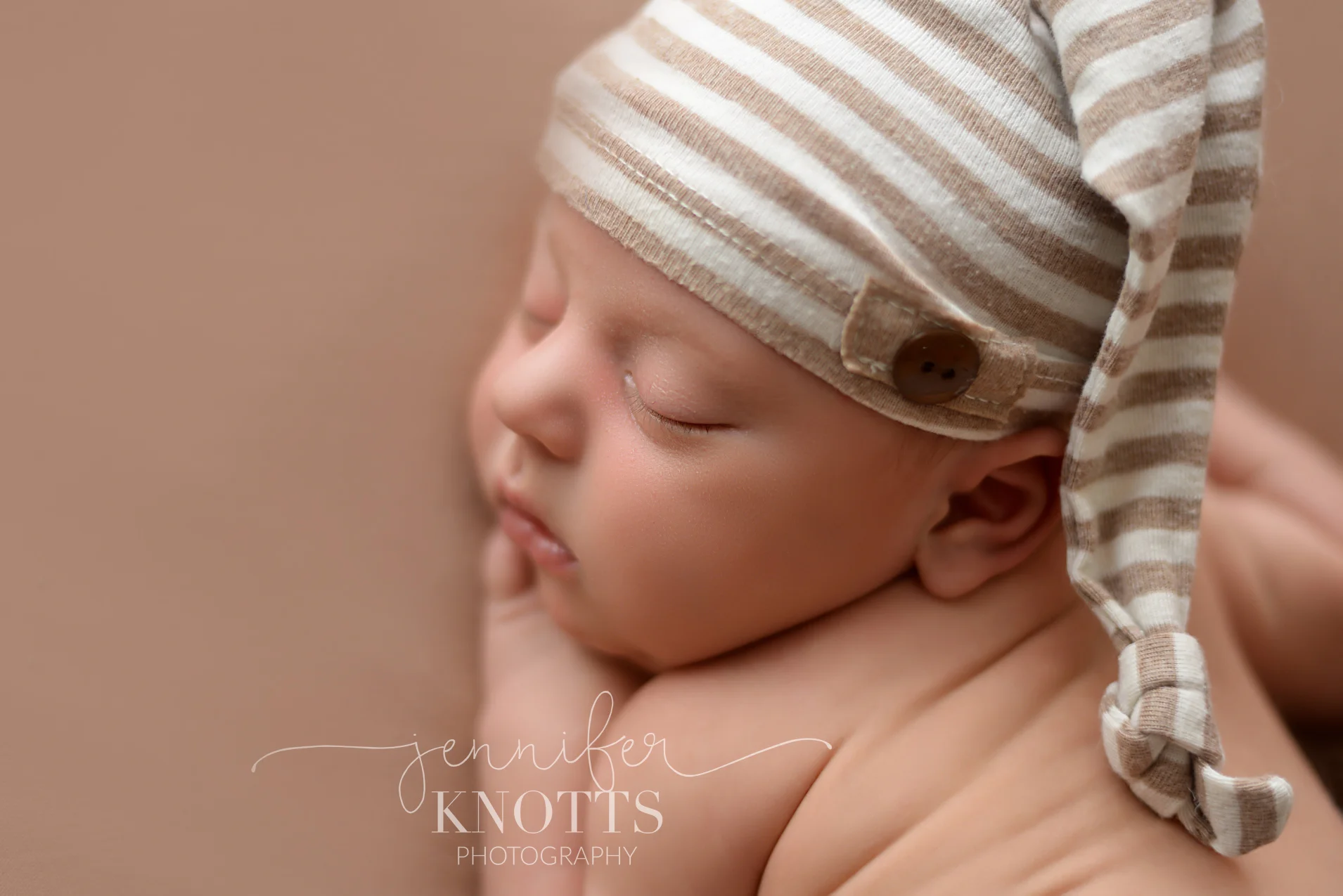 newborn boy wearing sleepy cap while posed with hand under cheek