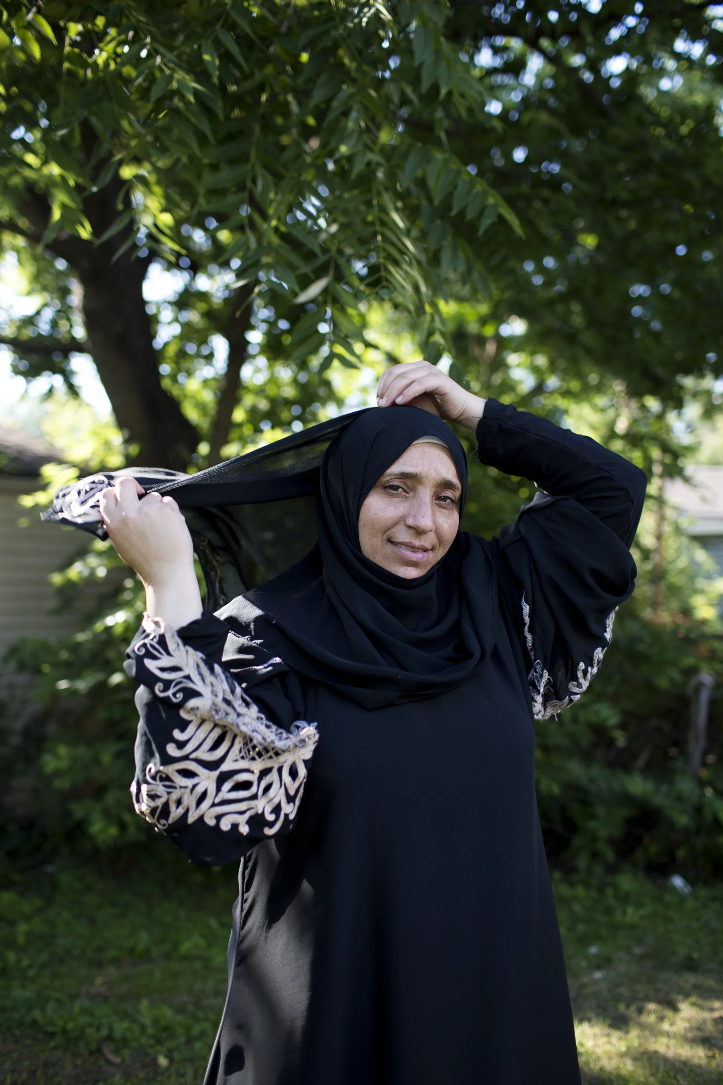 Mariam adjusts her hijab for a portrait in her backyard.