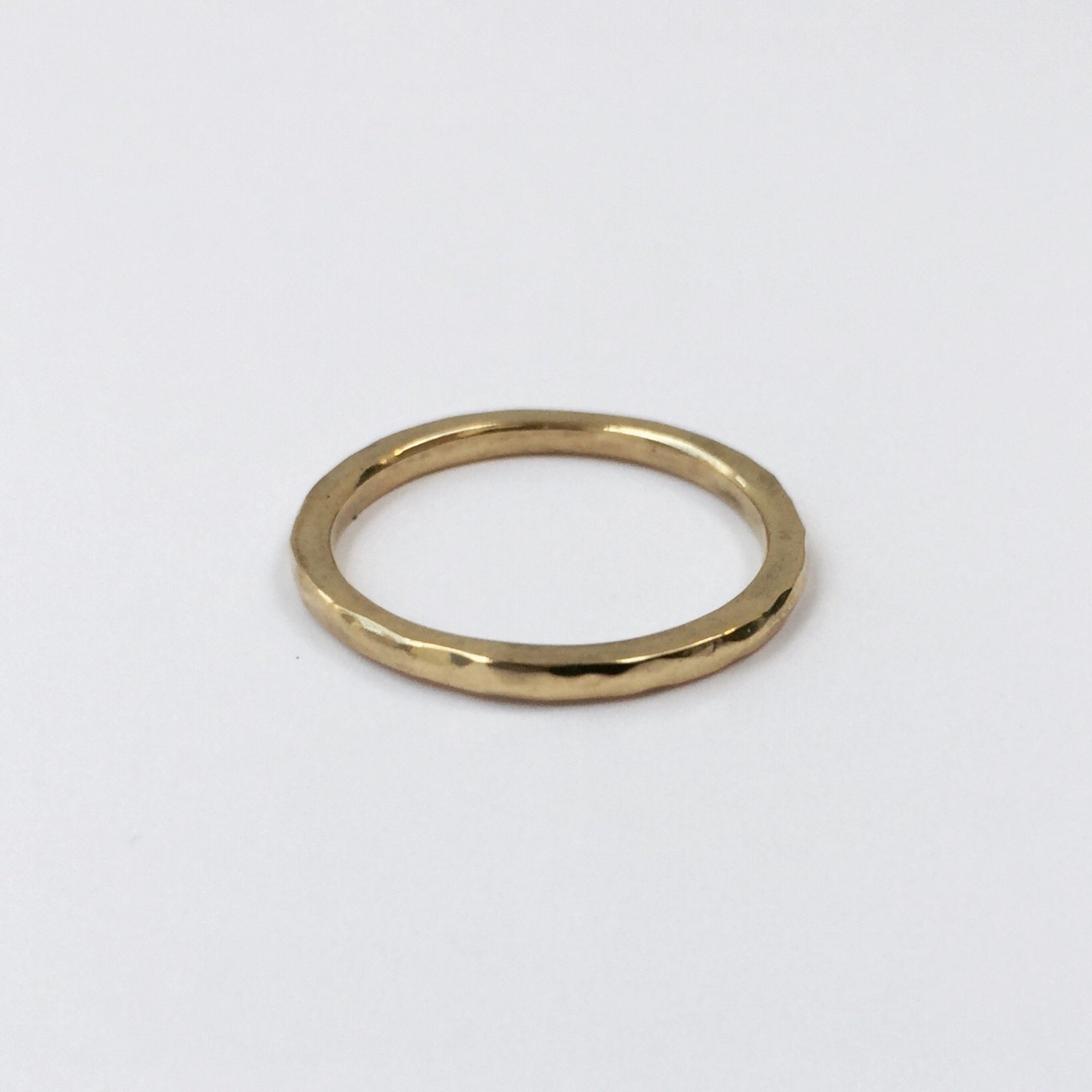 A gold ring with a slightly irregular, hand carved texture, placed on a plain white background.