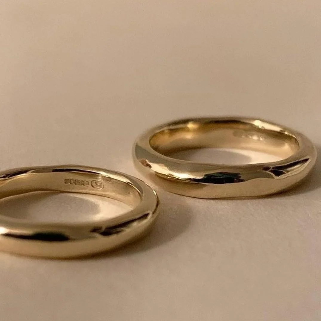 Two gold wedding bands on a light-colored surface.