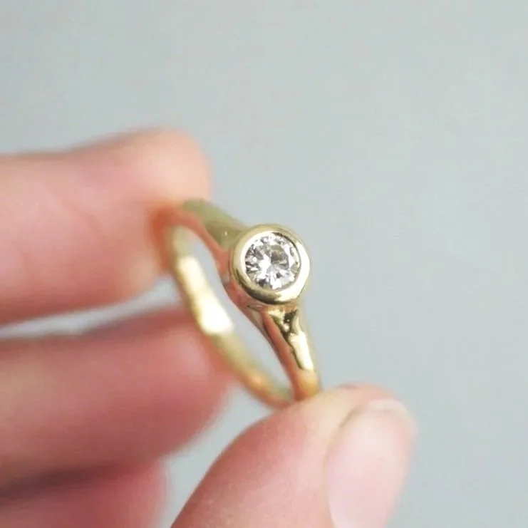 Gold ring with a round diamond set in the center, held between fingers.