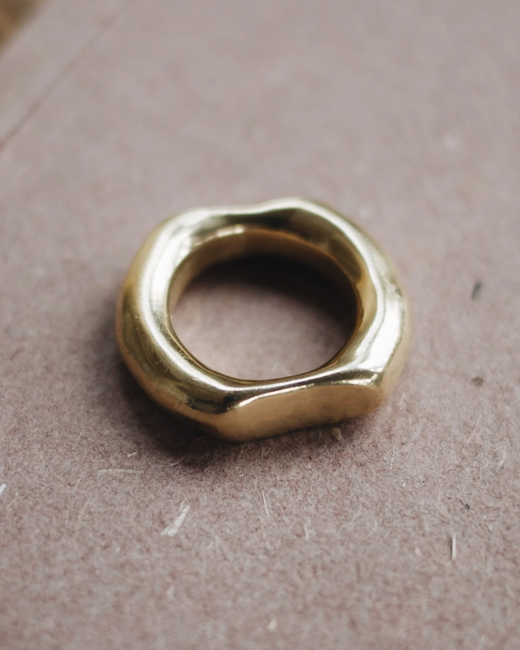 A gold ring with a uniquely shaped, irregular design resting on a brown surface.
