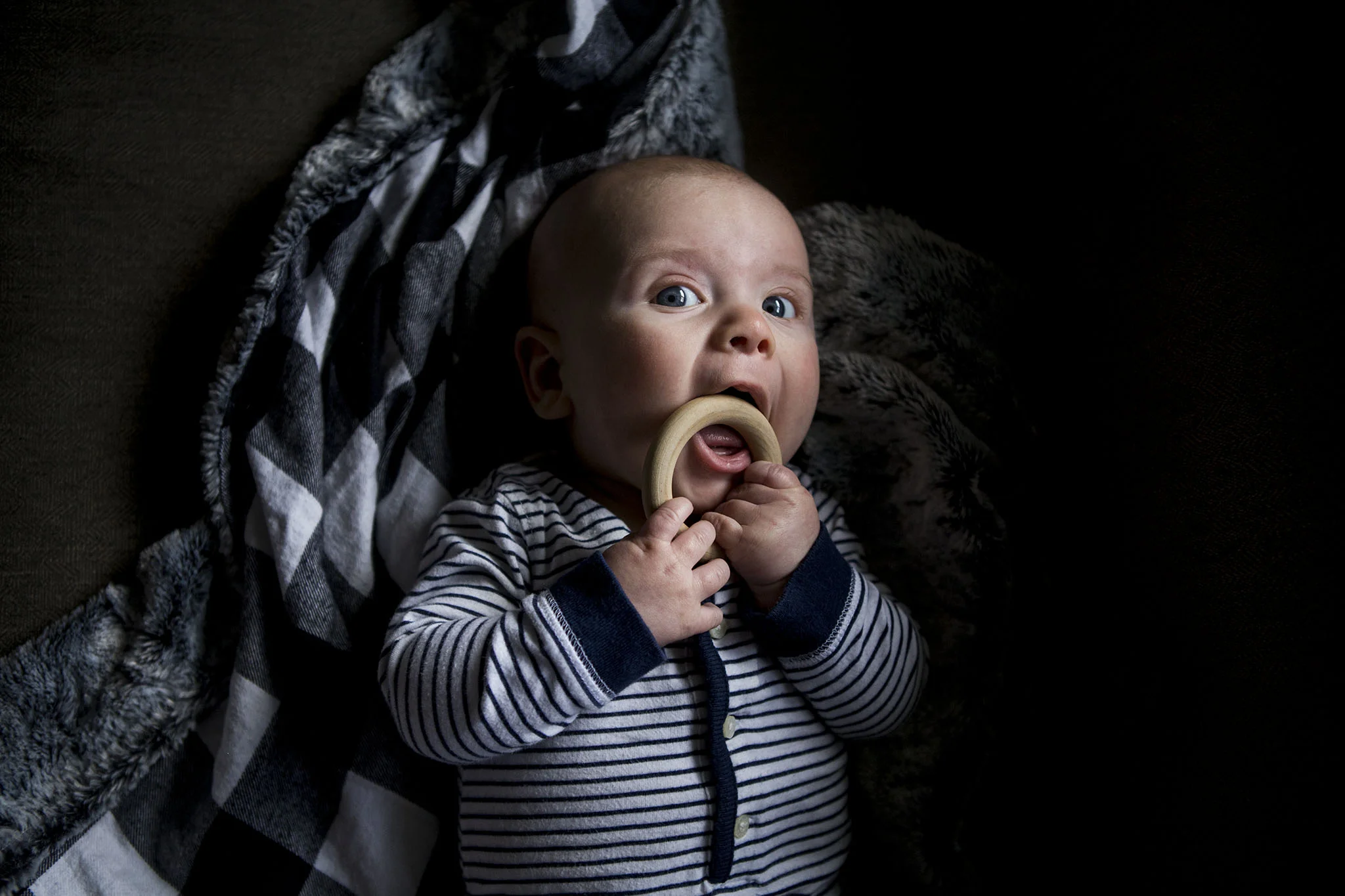 Authentic connecticut baby portraiture of baby chewing wooden teething ring, baby is 3 months old.