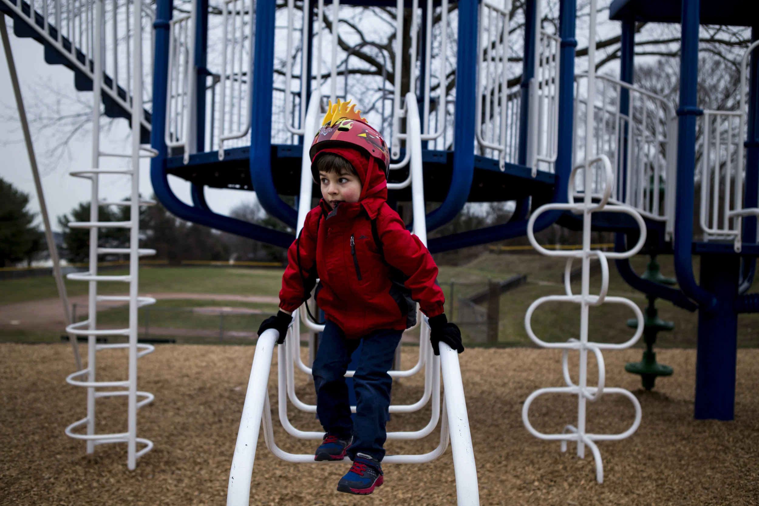 Candid environmental portrait of a child dressed in red, wearing a helmut climbing playground equipment by Connecticut child photographer specializing in authentic child portraiture.