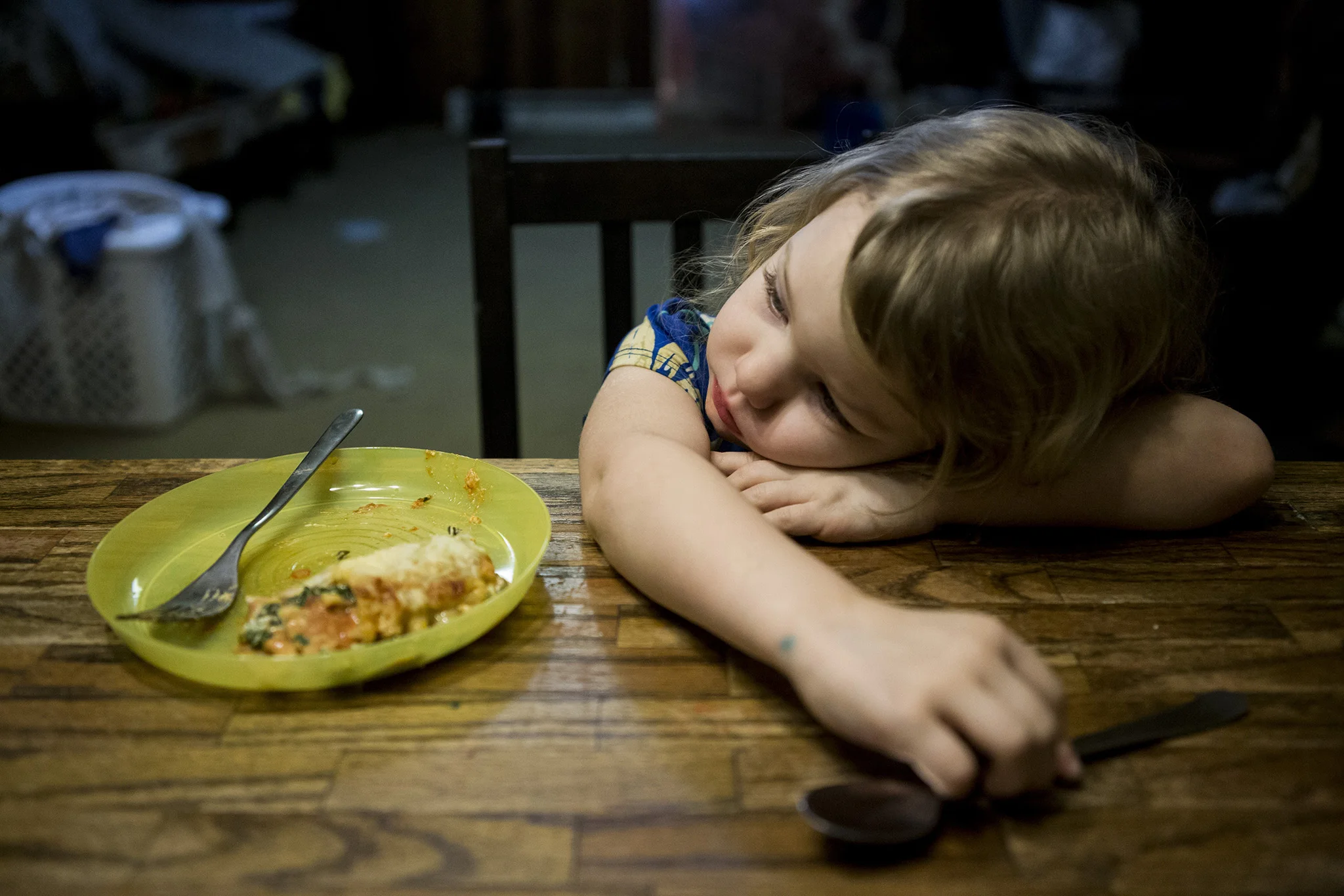 Real Life family pictures in Connecticut of a little girl who looks very tired laying her head on the dinner table with her half finished dinner sitting next to her.