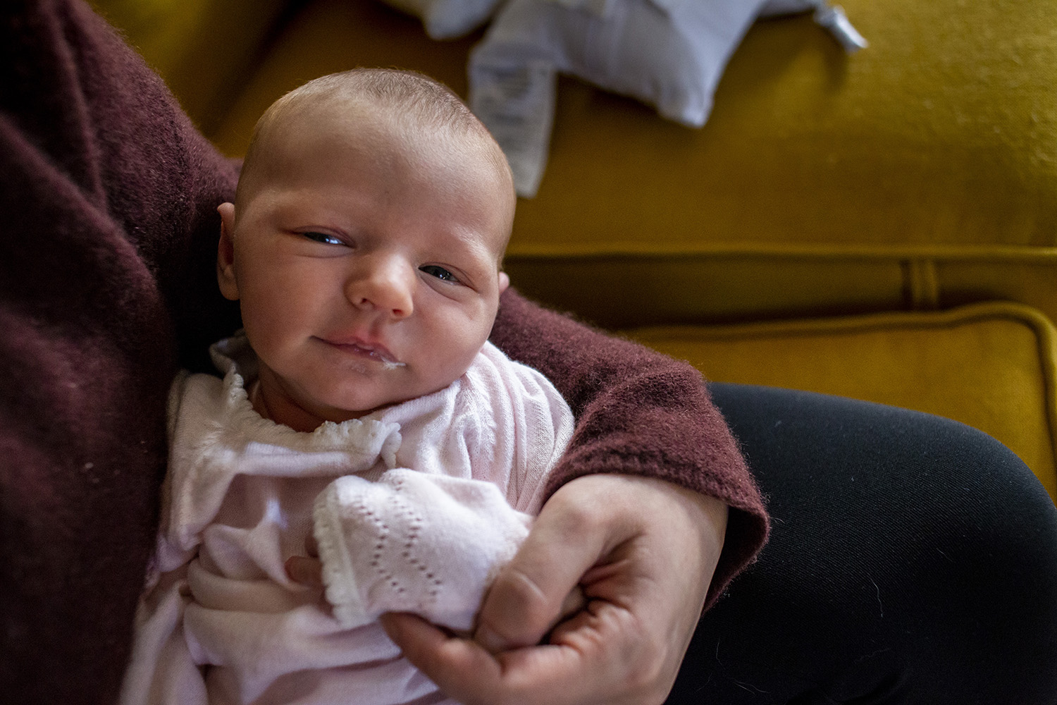 Boston newborn smiles subtly with dribble of milk in the corner of her mouth.