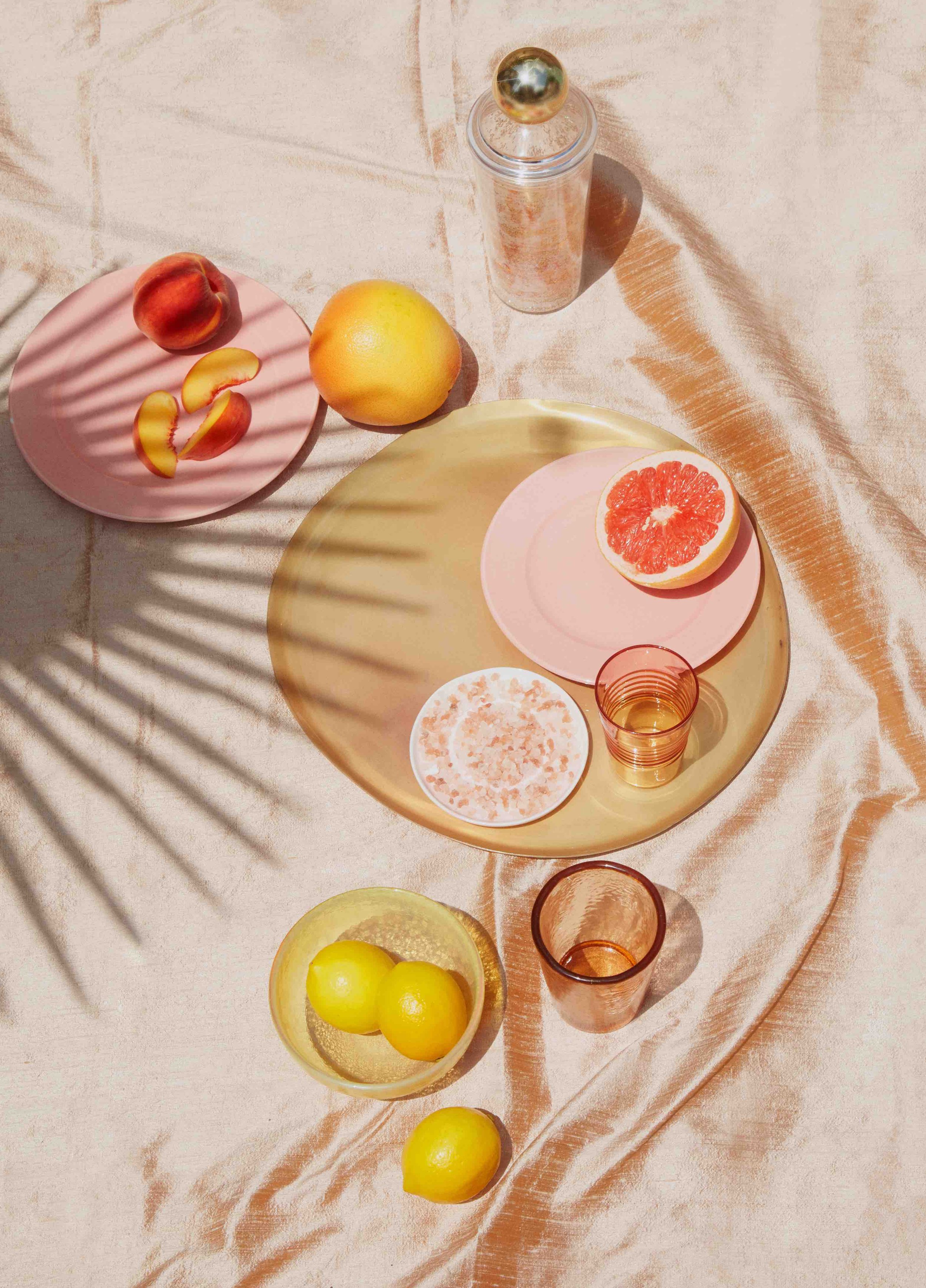 palm leaf shadow on a picnic of citrus snacks and pink plates.jpg