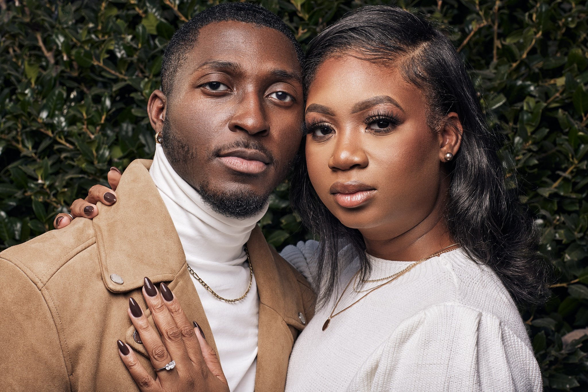 couple pose in front of a green bush during their engagement session