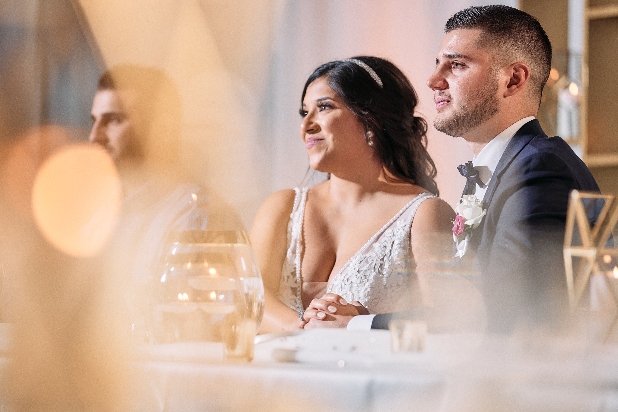 a bride and groom listen to a toast during their wedding reception