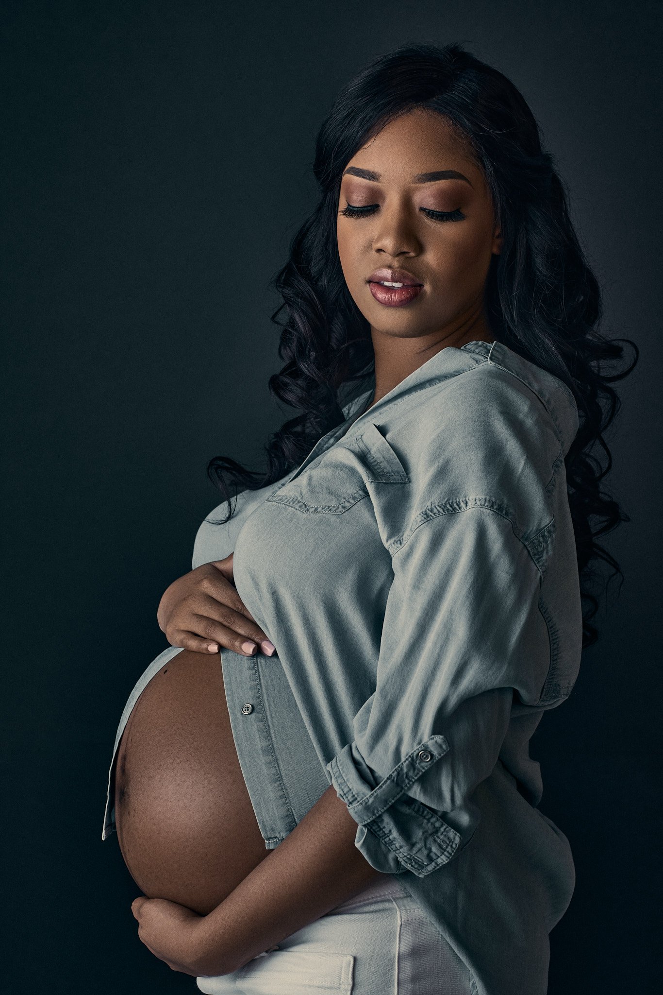 pregnant woman poses in front of a dark background