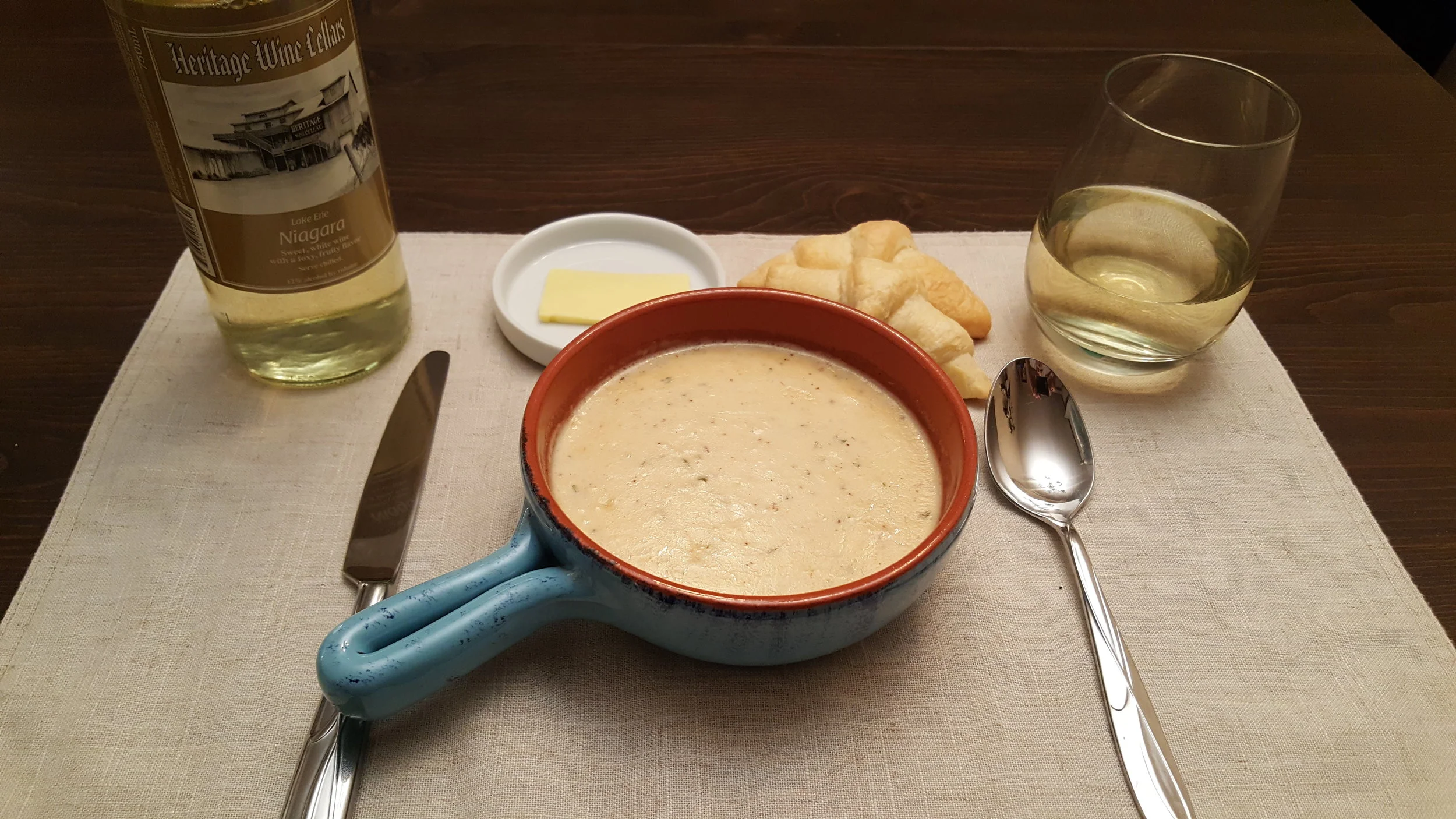 A bowl of Damn Good Crab Bisque served as it should be. With a Lake Erie Niagara Wine & buttery crescent rolls.