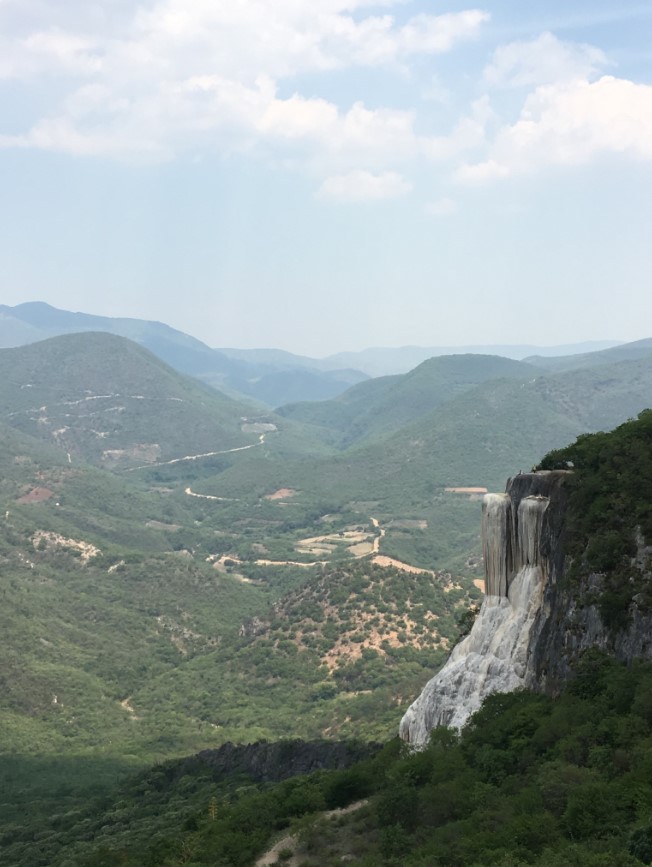 "Hierve el Agua" translates to “the water boils”, and the natural mineral springs that are found here take their name from the bubbling of the warm water as it flows up from the earth through the springs and releases oxygen into the turquoise cliff-top pools. What appears to be a massive waterfalls frozen to the side of the mountain are actually natural mineral formations that have built up over thousands of years as a result of the mineral-laden water spilling over the edge of the cliff and trickling down the rocky mountain side. Photo on the left is from a higher peak looking down to what we hiked to (photo below) In the photo below, you can see how large this formation is by looking at the small 2 people at the base (look hard…)