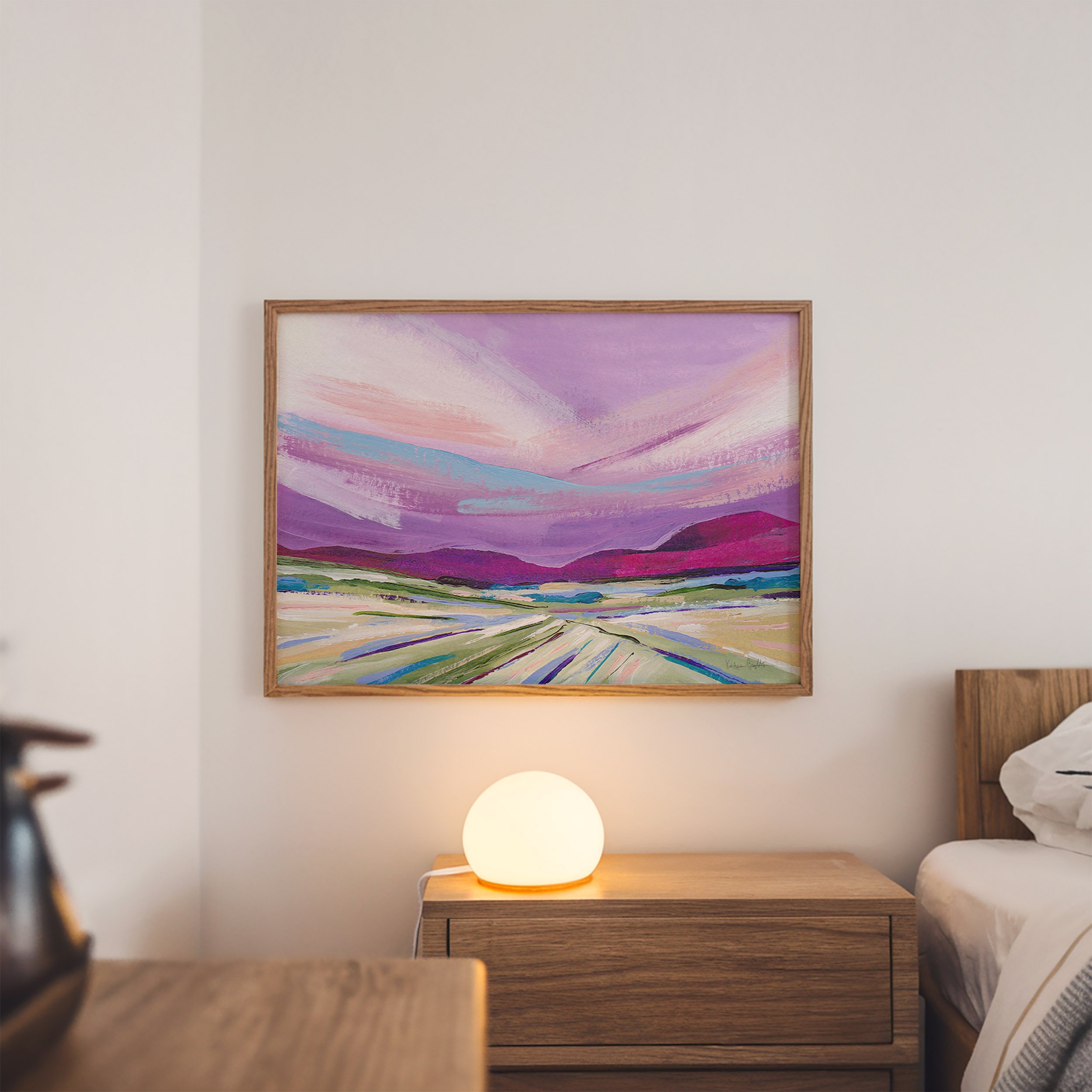 Abstract painting of a landscape with a purple sky, pink and blue clouds, and green and purple hills. The painting is framed in a light wood frame. Art by Kendra Castillo