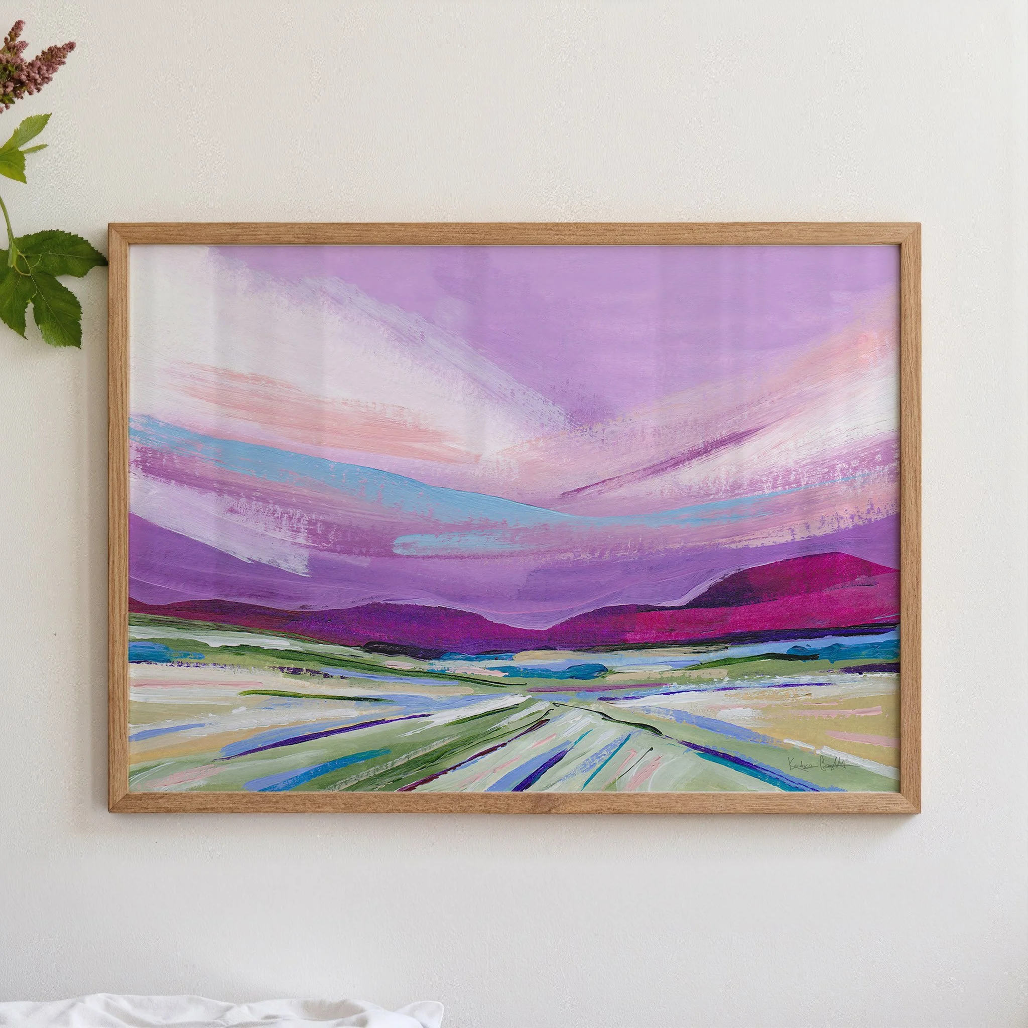 Abstract painting of a landscape with a purple sky, pink and blue clouds, and green and purple hills. The painting is framed in a light wood frame. Art by Kendra Castillo