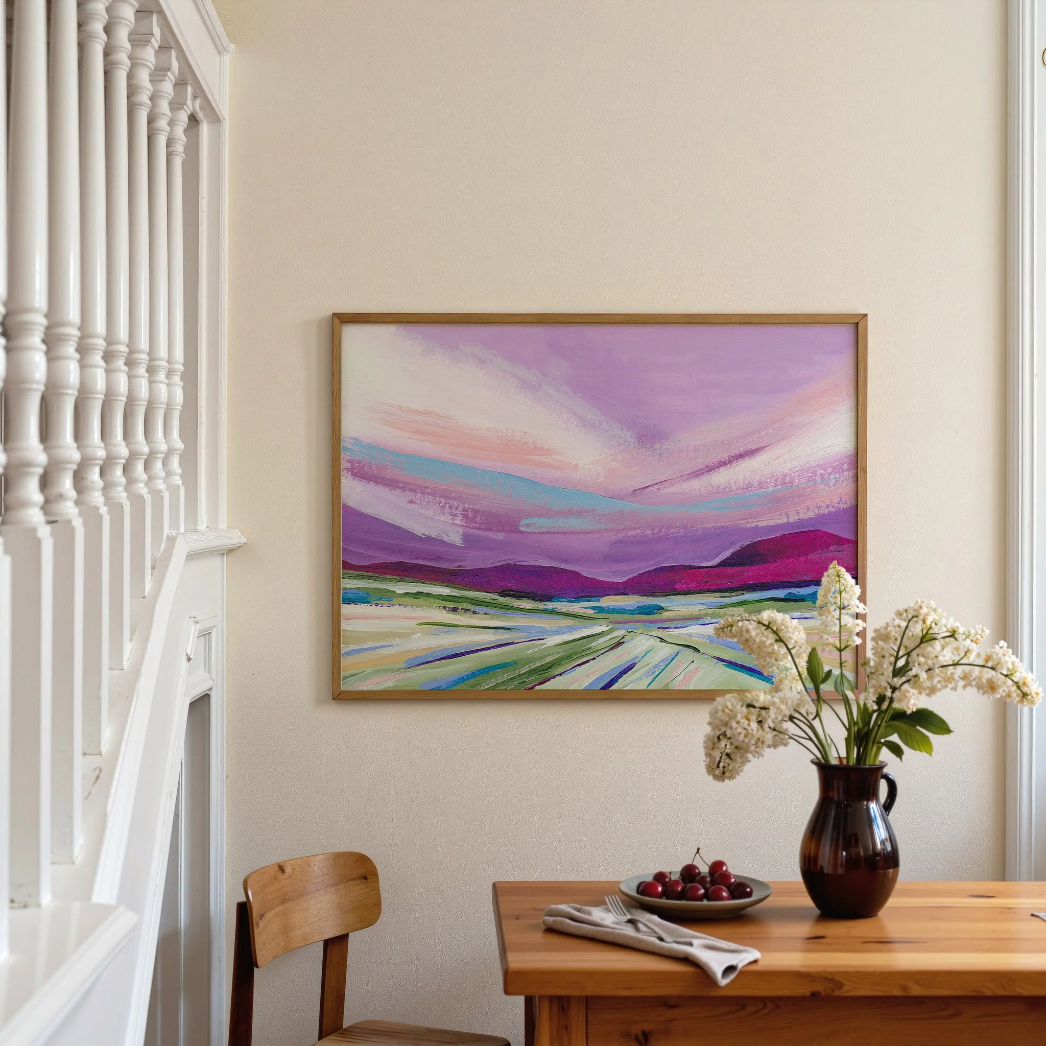 Abstract painting of a landscape with a purple sky, pink and blue clouds, and green and purple hills. The painting is framed in a light wood frame. Art by Kendra Castillo