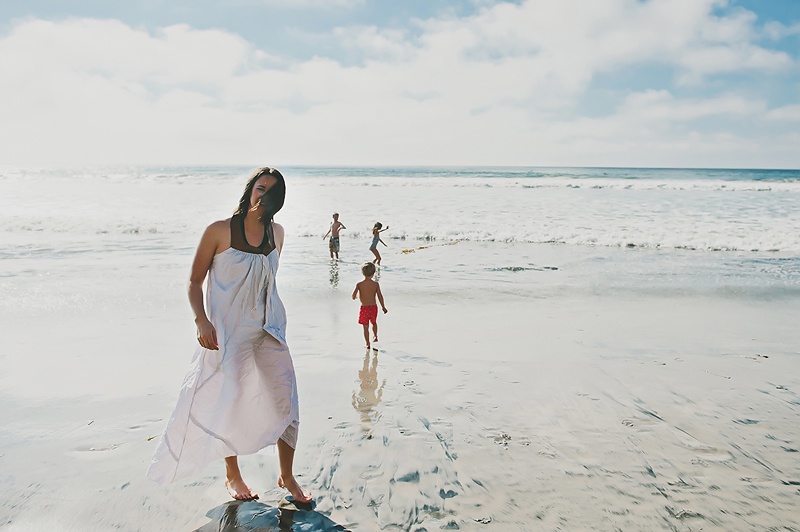 woman in dress on beach kids playing in ocean