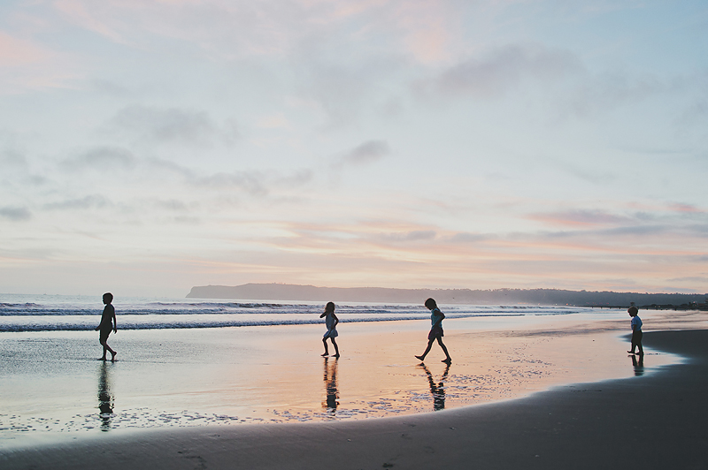 four kids walking on beach at sunset